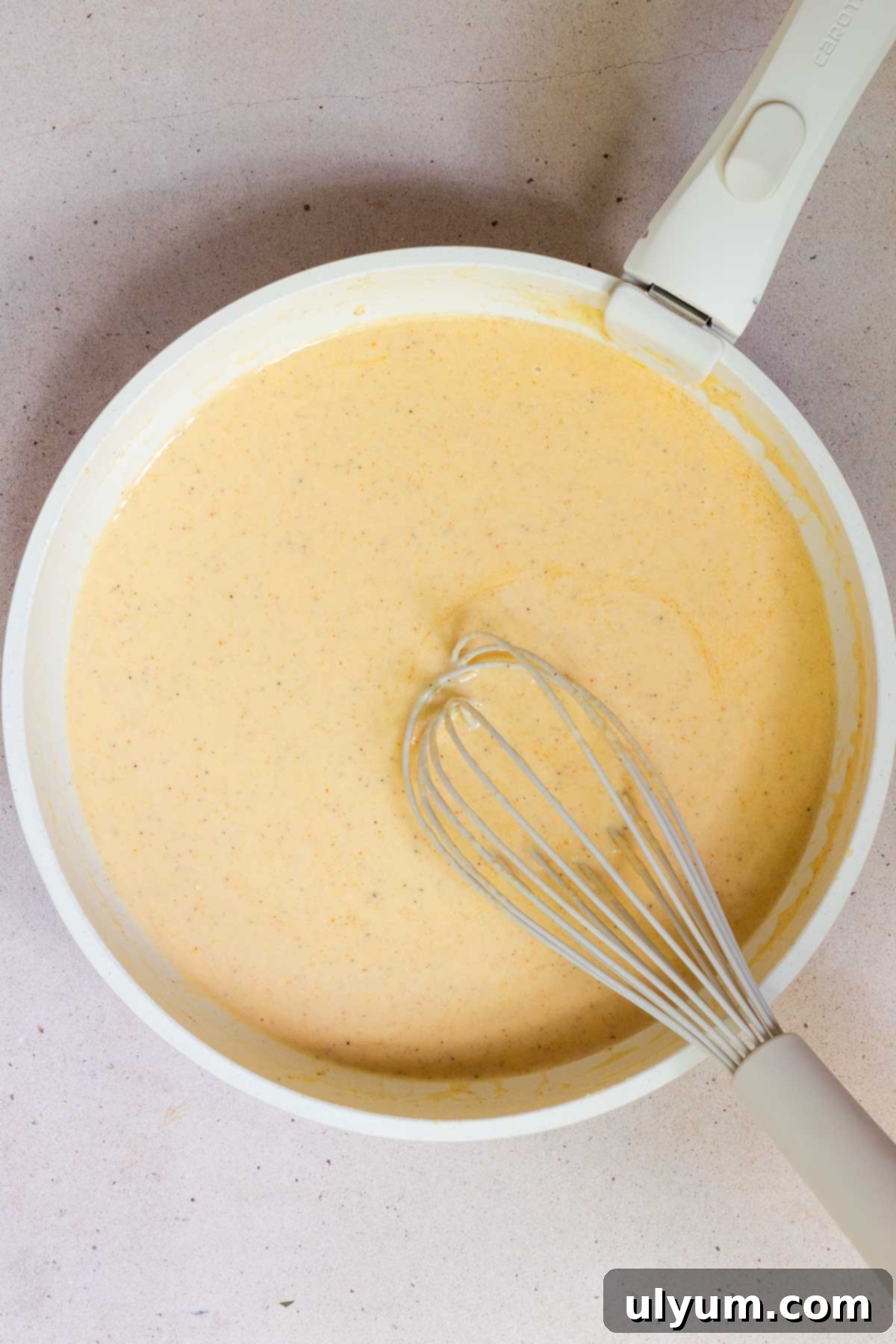 Cajun Alfredo sauce being whisked until smooth in a large skillet.