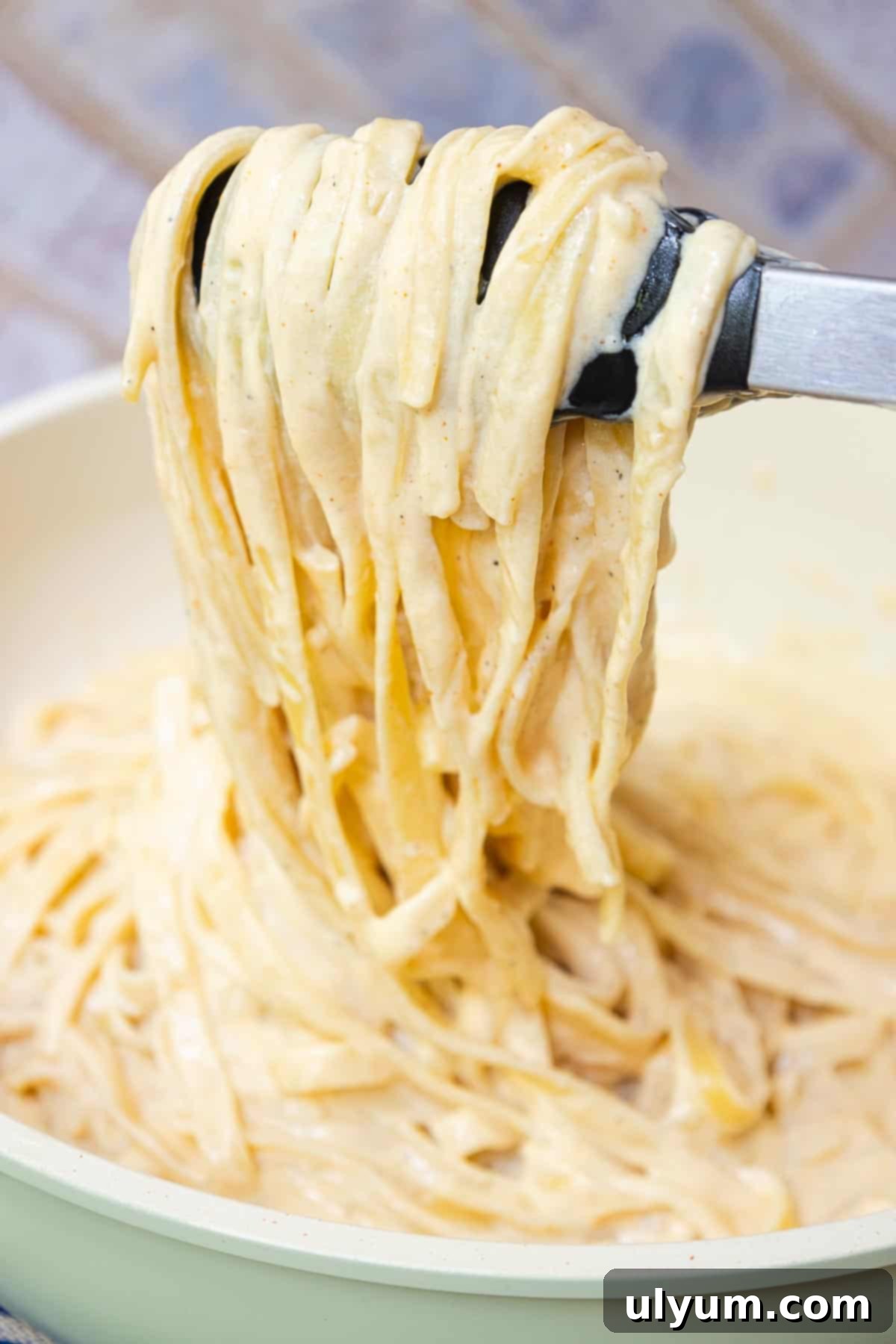 Cooked fettuccine being mixed in with creamy Cajun Alfredo sauce with tongs.