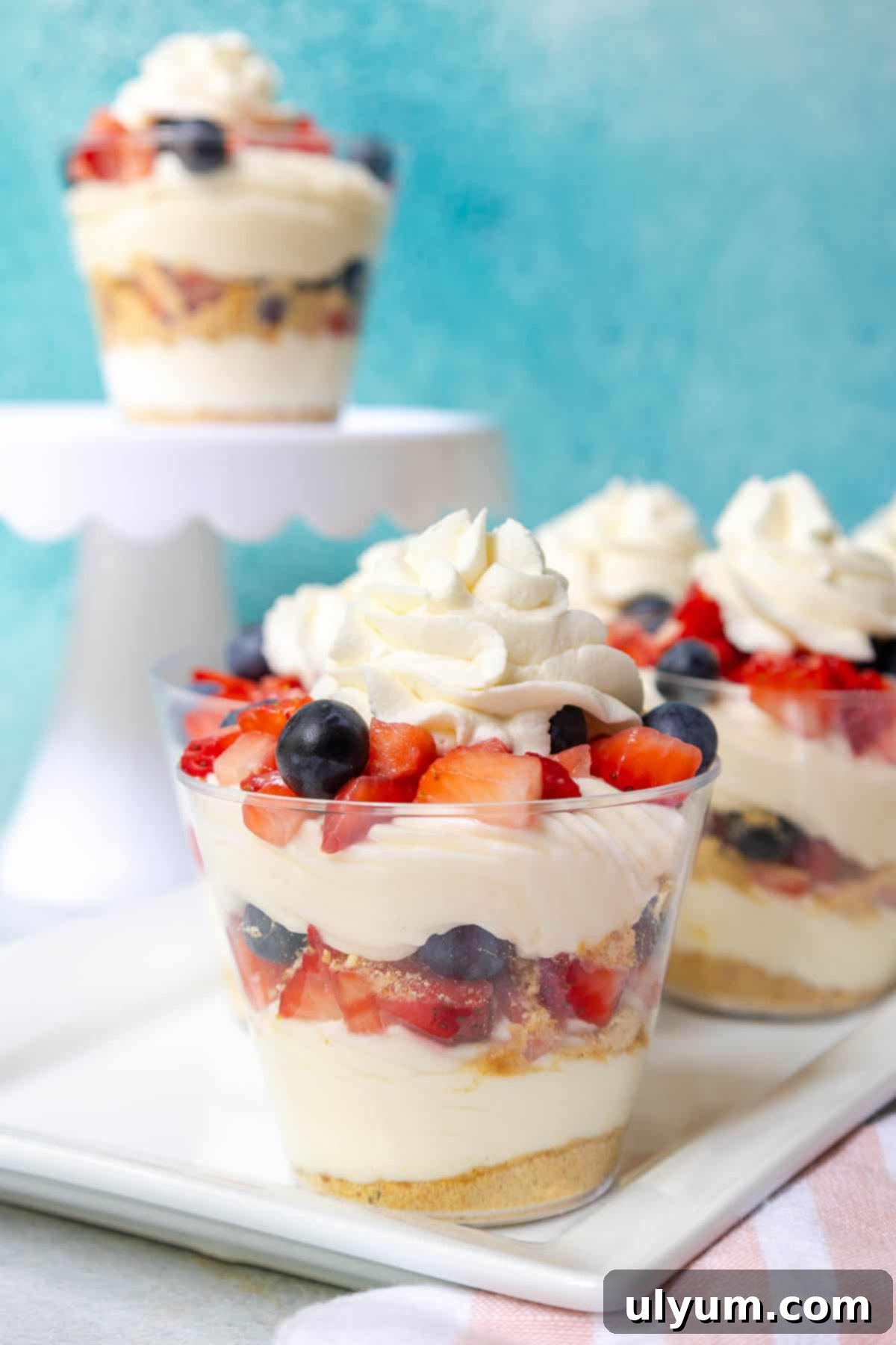 Layered no bake cheesecake cups with repeating layers of crust, cream cheese mixture, fresh blueberrie and diced strawberries, and whipped cream.