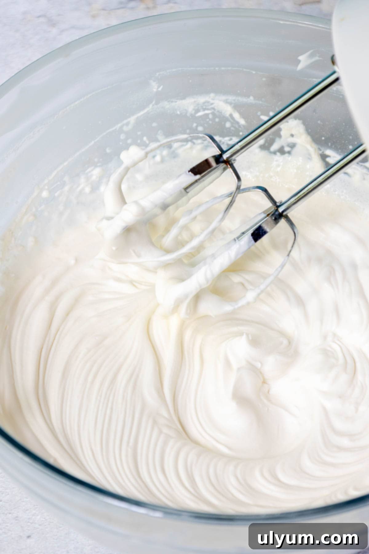 In a large mixing bowl, the heavy cream is whipped with a hand mixer until stiff peaks form to create whipped cream.