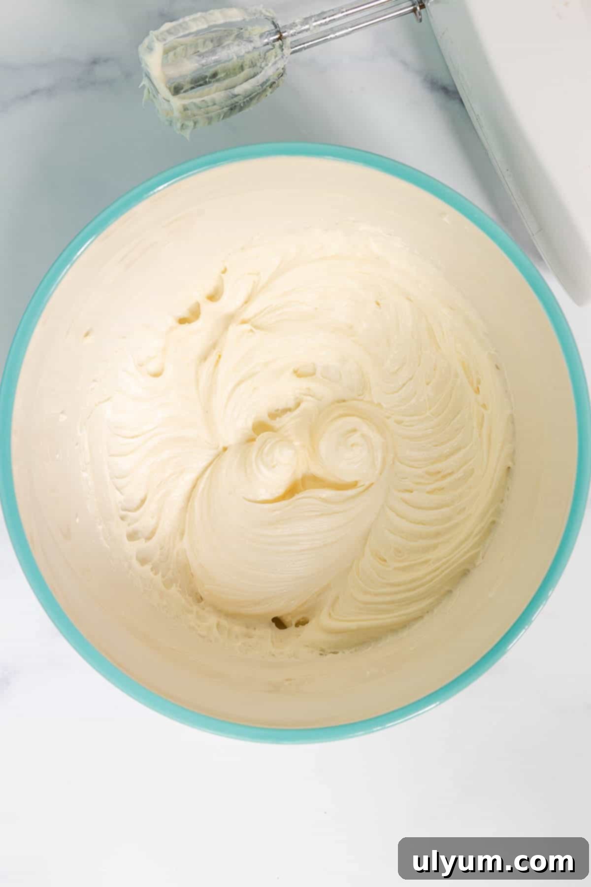 In a large mixing bowl, the softened cream cheese and sugar are combined with a hand mixer until smooth.