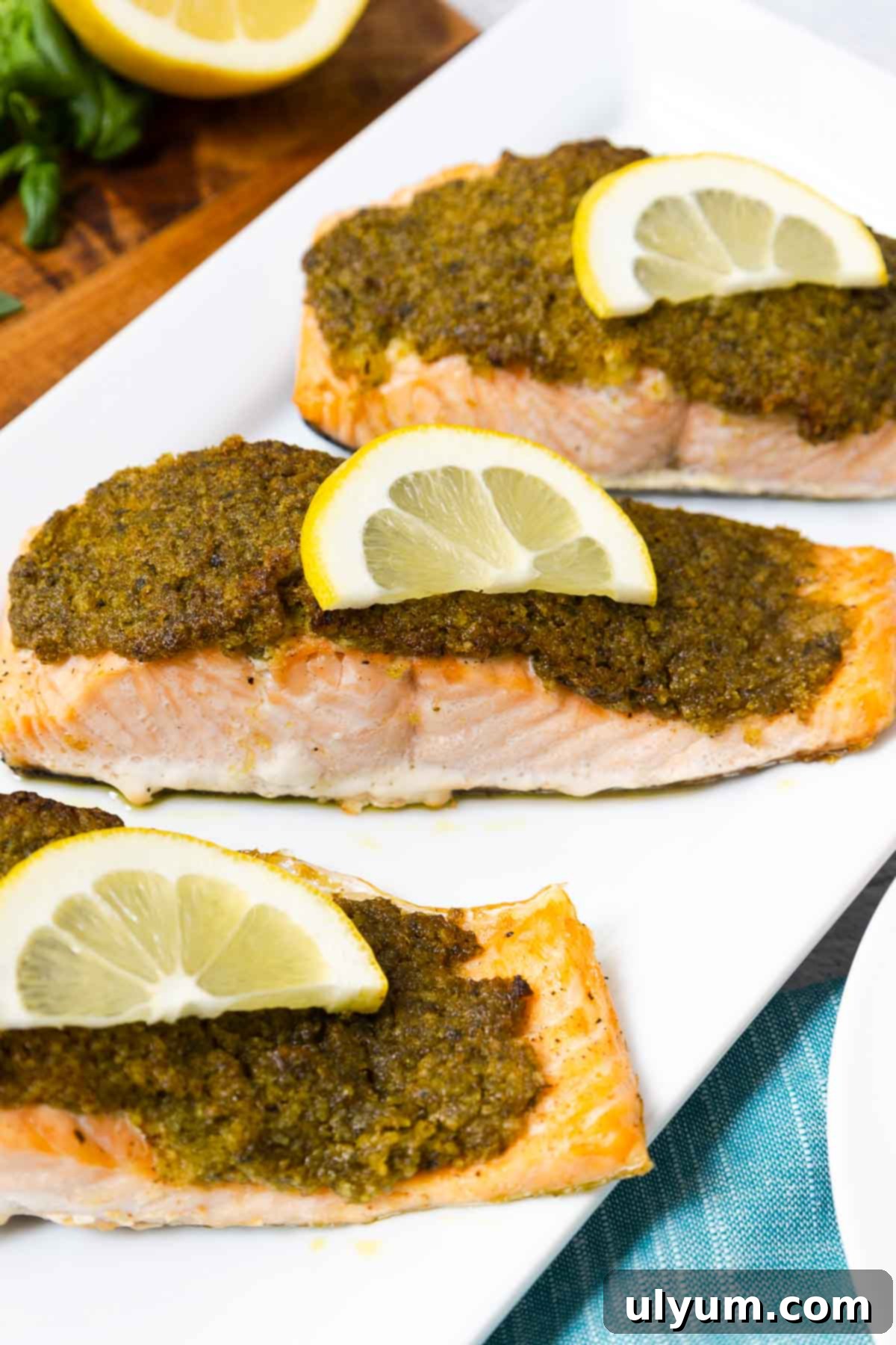 Three salmon fillets topped with pesto crust and slice of lemon, ready to be served.