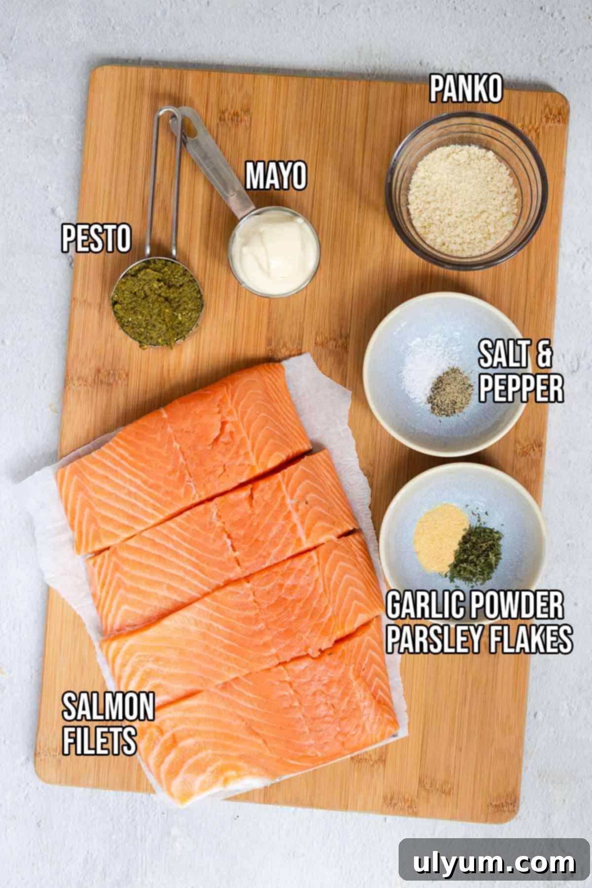 Pesto crusted salmon ingredients laid out: salmon fillets, pesto, mayo, panko, garlic powder, parsley flakes, salt, and pepper.