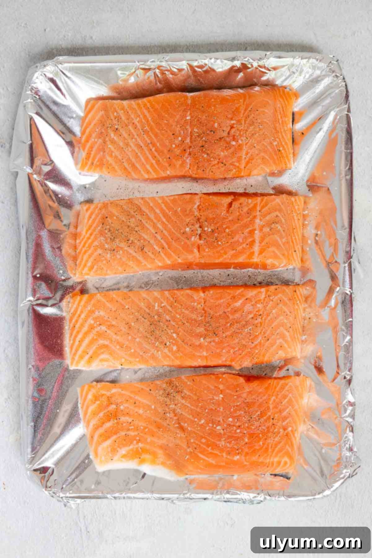 Four salmon fillets are seasoned with salt and pepper evenly before baking.