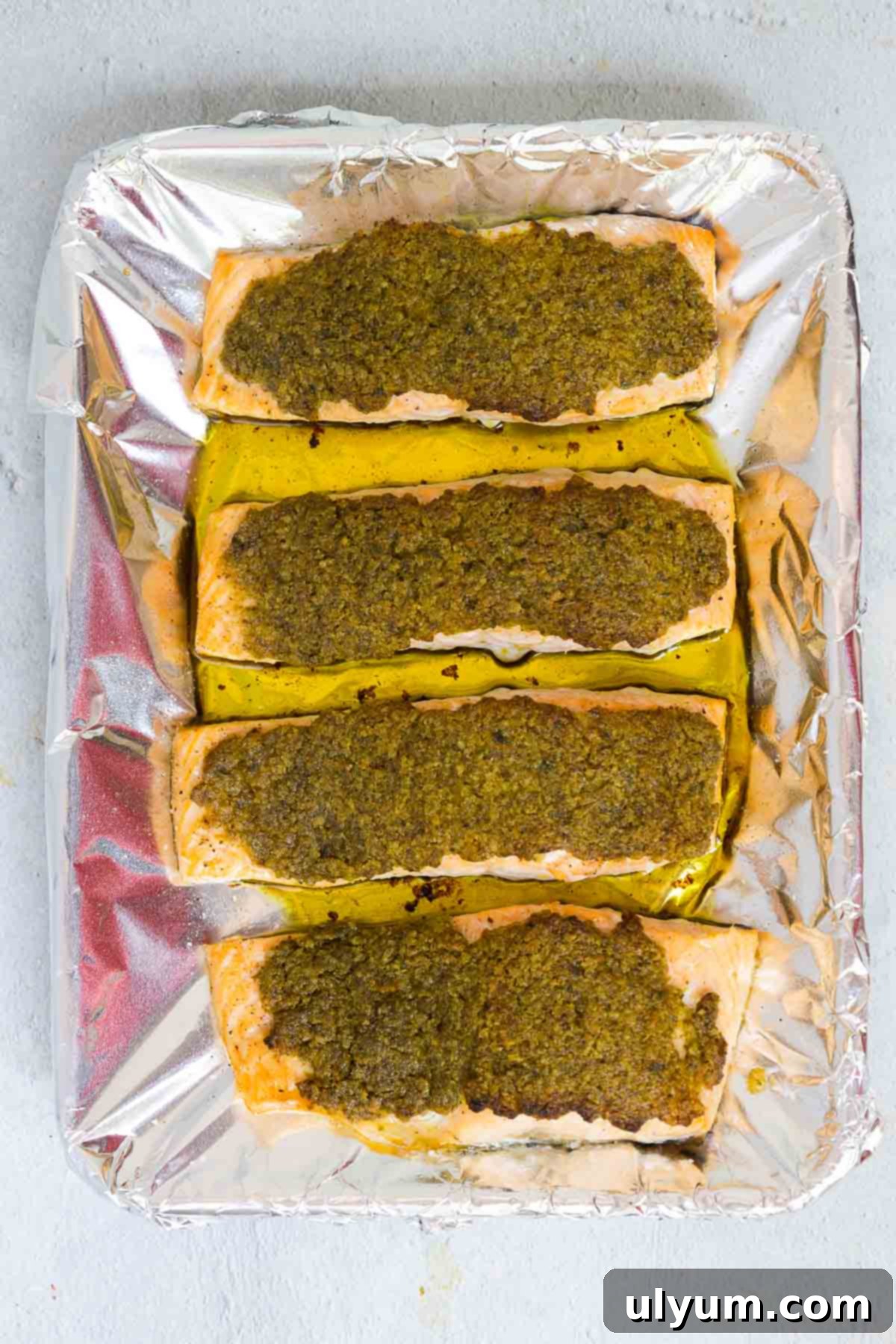 Four pesto crusted salmon fillets baked on a baking tray covered in foil until opaque and golden