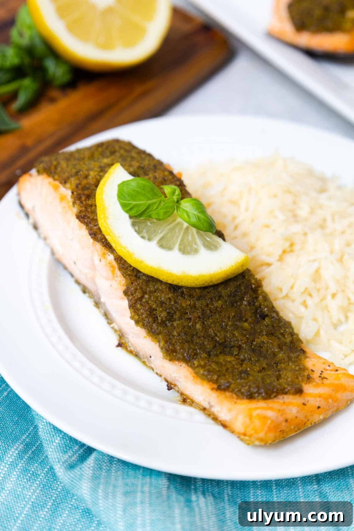 A single salmon fillet topped with a generous pesto layer and a fresh slice of lemon, ready to be served on a plate.