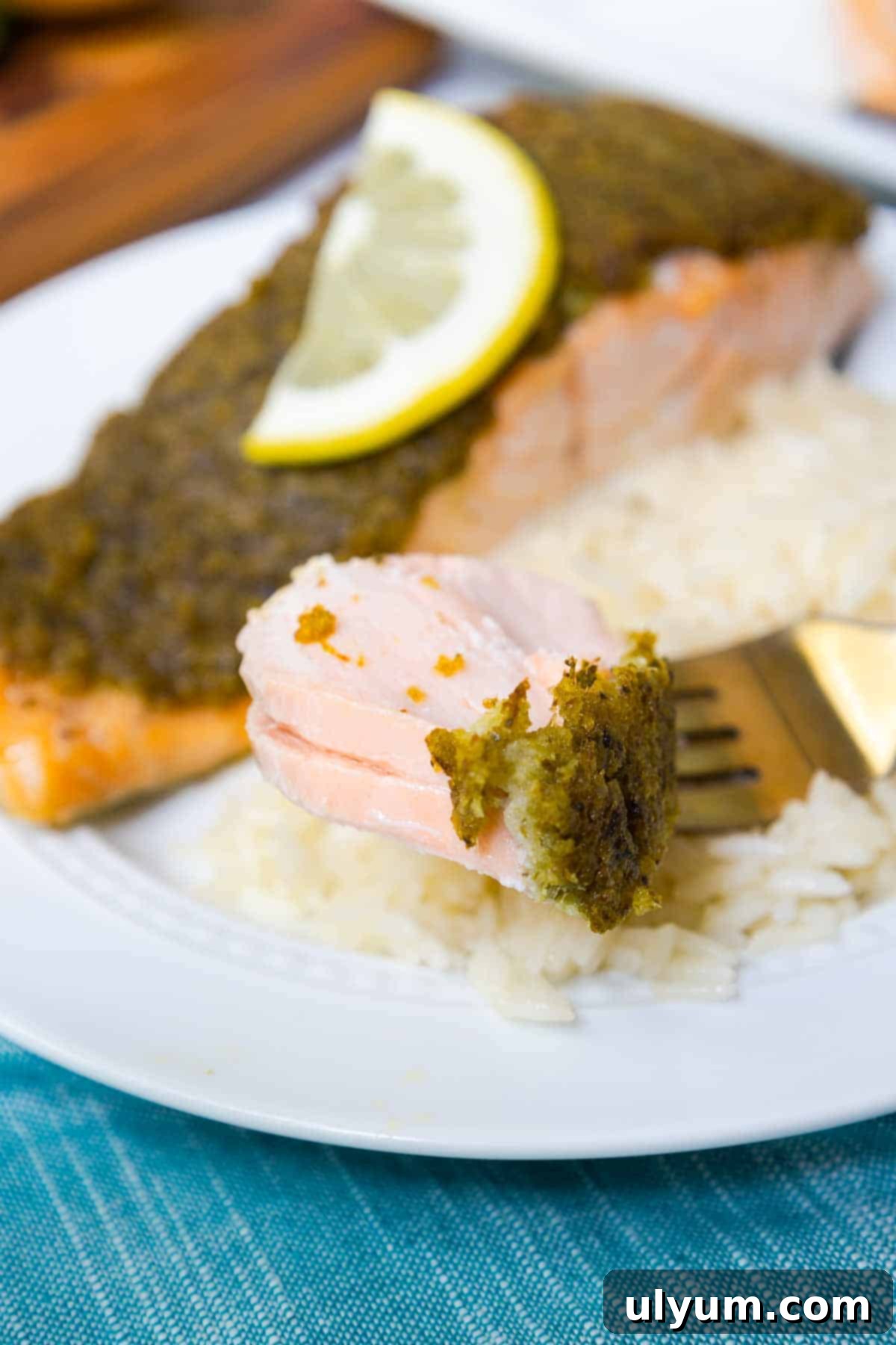 A forkful of pesto crusted salmon shows flaky layers of fish, highlighting its tender texture.