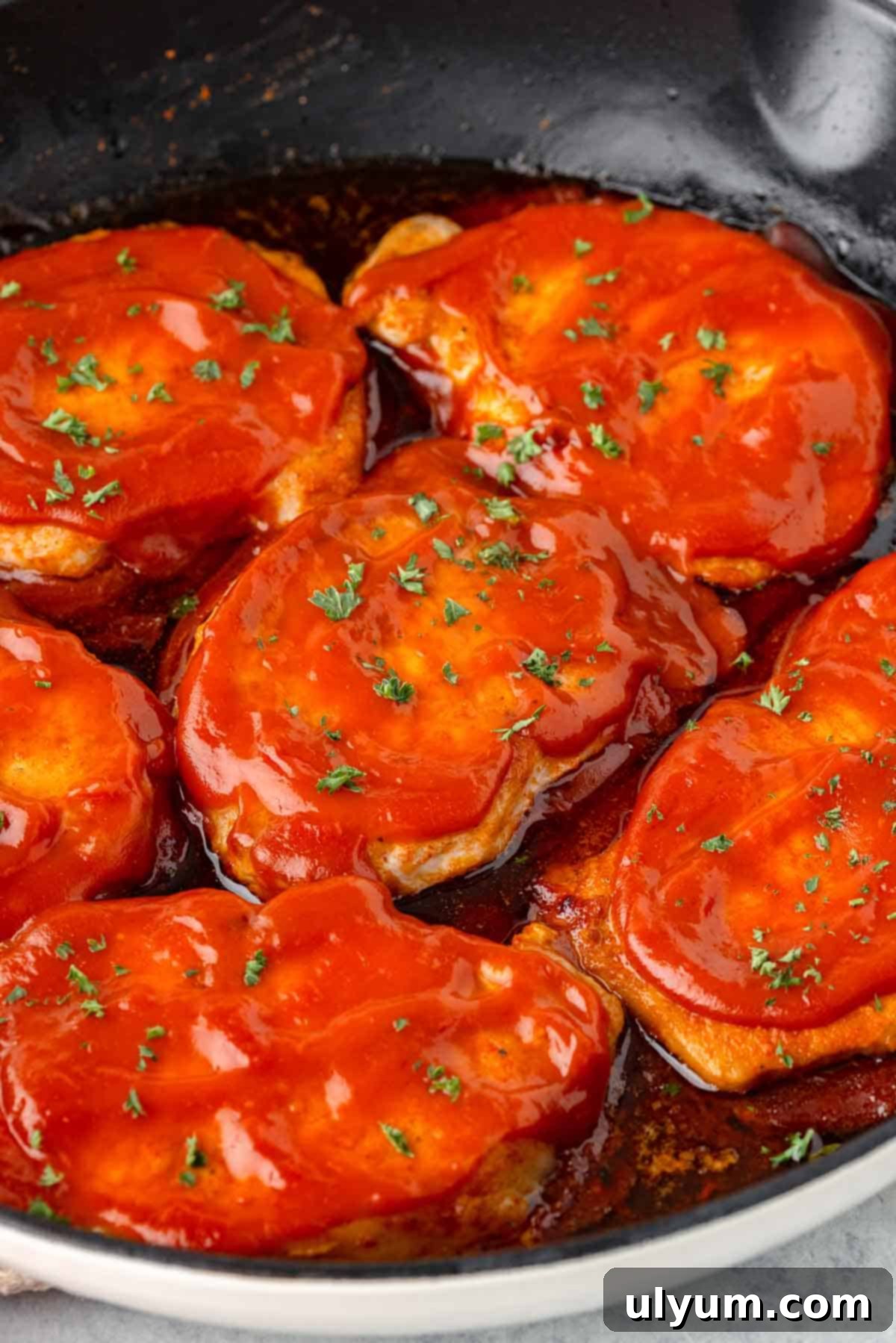 Boneless pork chops coated in BBQ sauce in a large skillet.