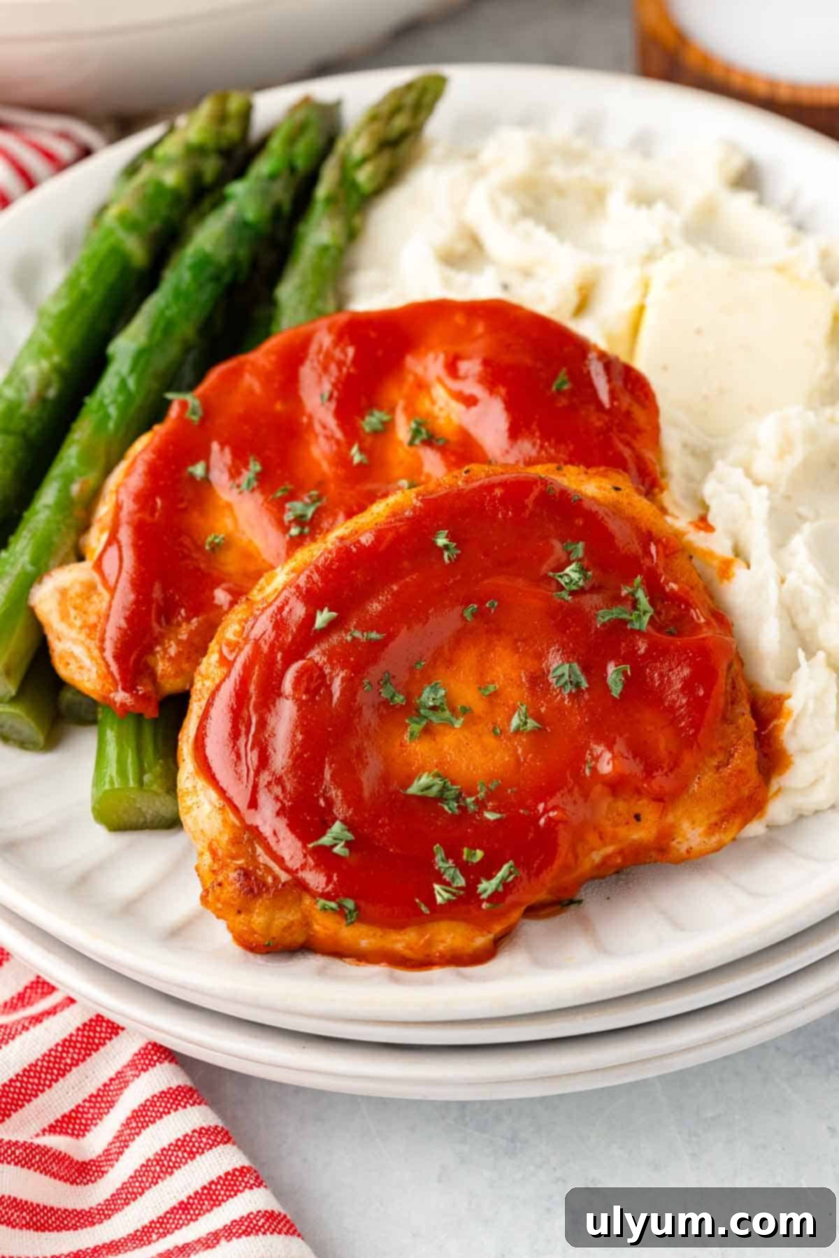 Boneless pork chops coated in BBQ sauce on a dinner plate with mashed potatoes and asparagus.