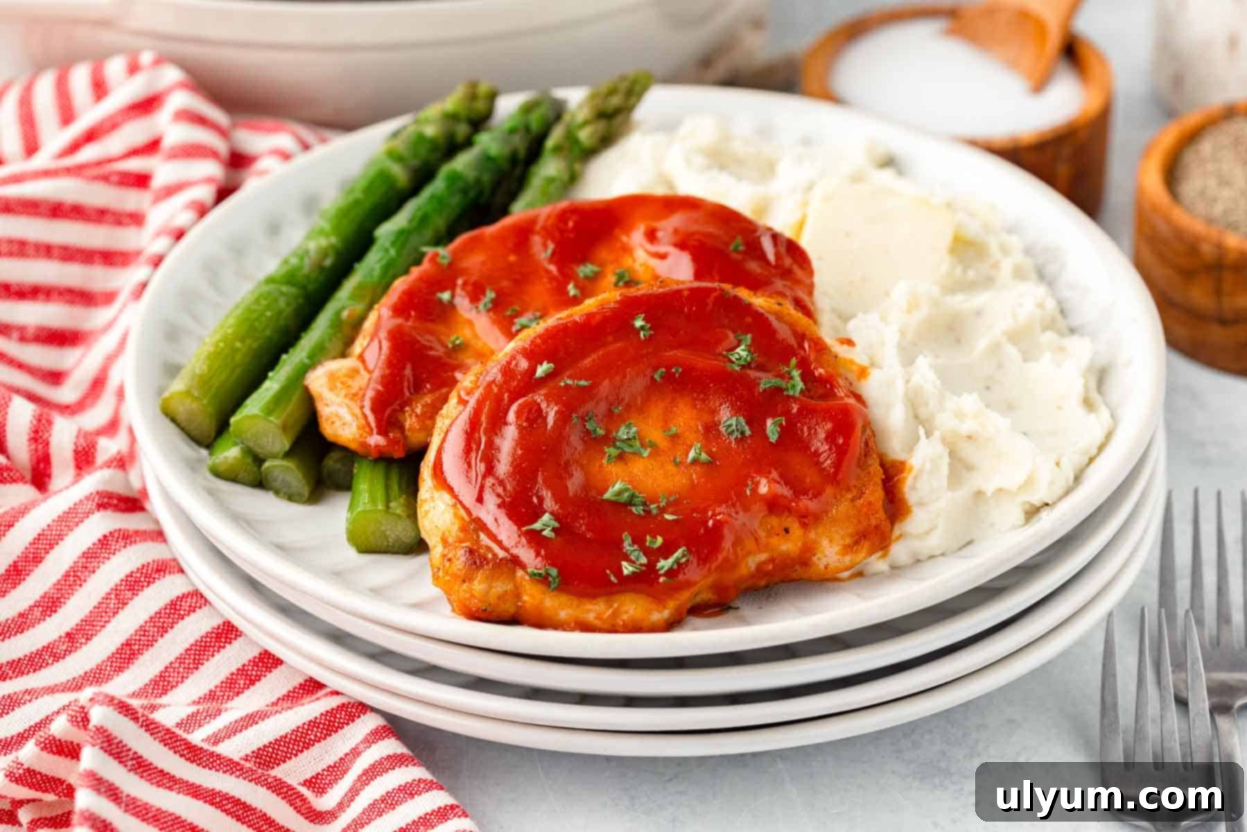 Boneless pork chops coated in BBQ sauce on a dinner plate with asparagus and mashed potatoes.