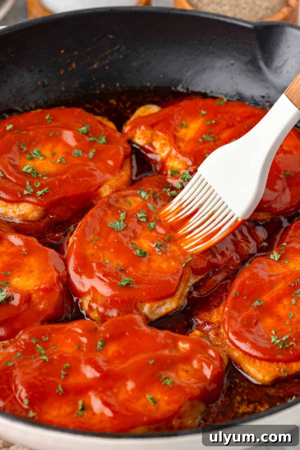 Boneless pork chops being basted with BBQ sauce in a large skillet.