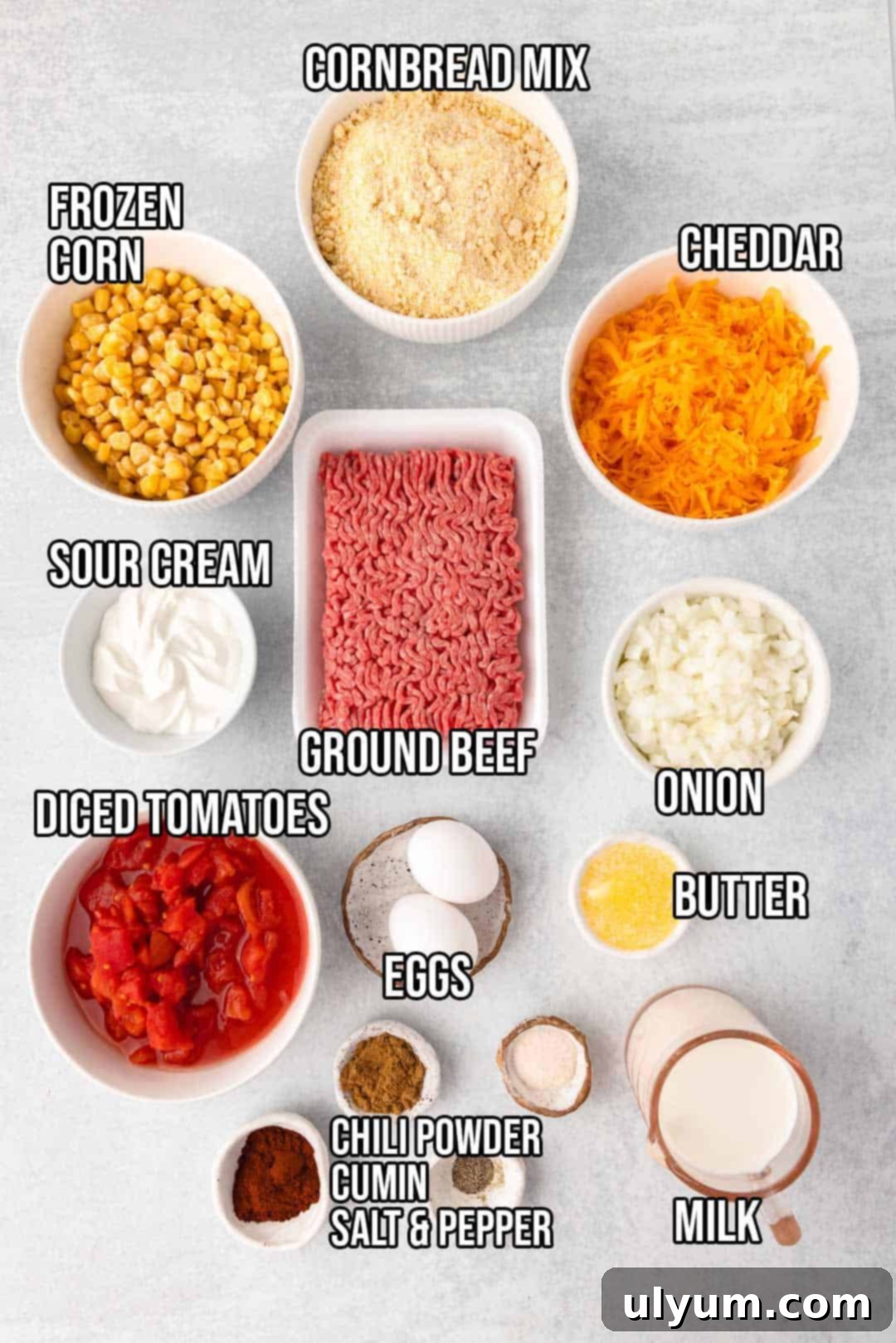 Cornbread mix, Ground beef, Onion, Corn, shredded Cheddar cheese, Diced tomatoes Drained, Eggs, Whole milk, Sour cream, melted Butter, Chili powder, ground cumin, garlic salt, and pepper — ingredients for a hearty casserole.