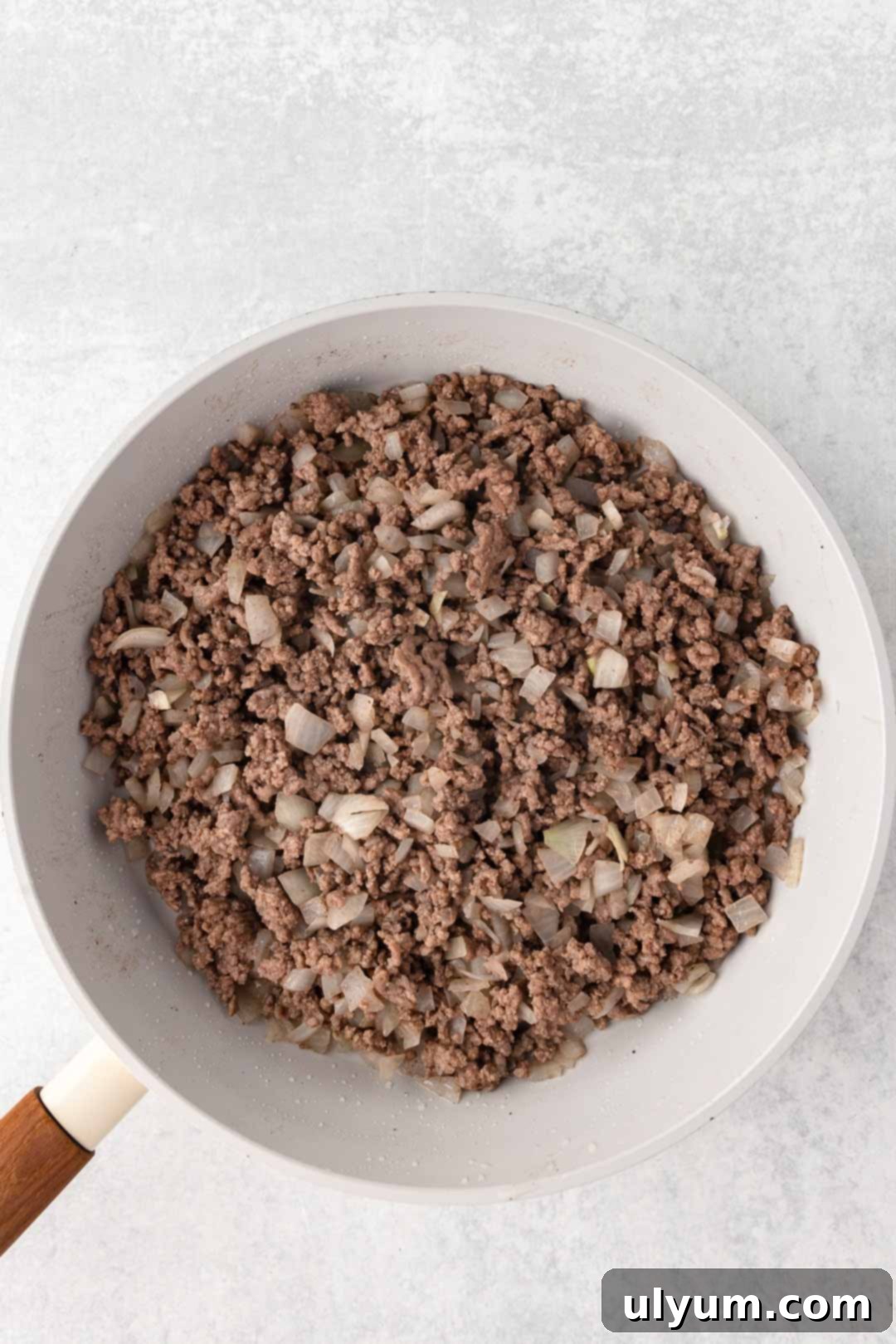 Browned ground beef and cooked diced onions in a large skillet, ready for seasoning.