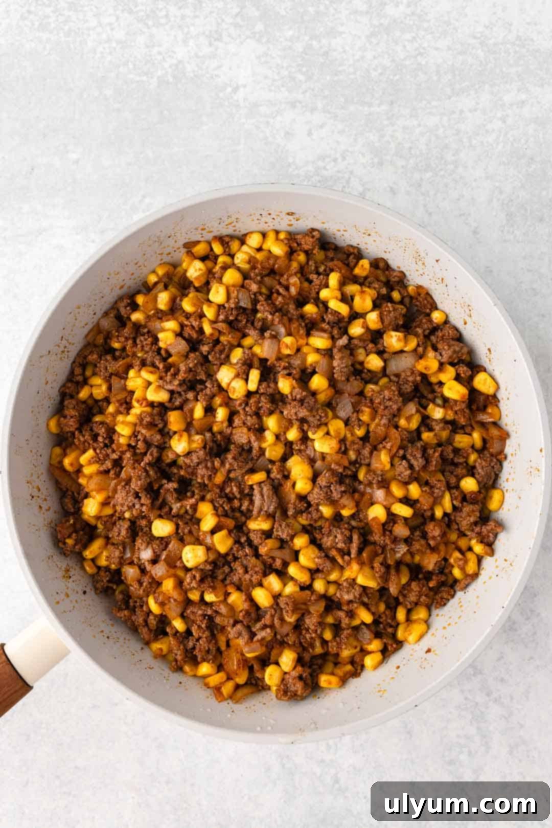 Ground beef, onion, and corn mixture stirred together in a large skillet with spices.