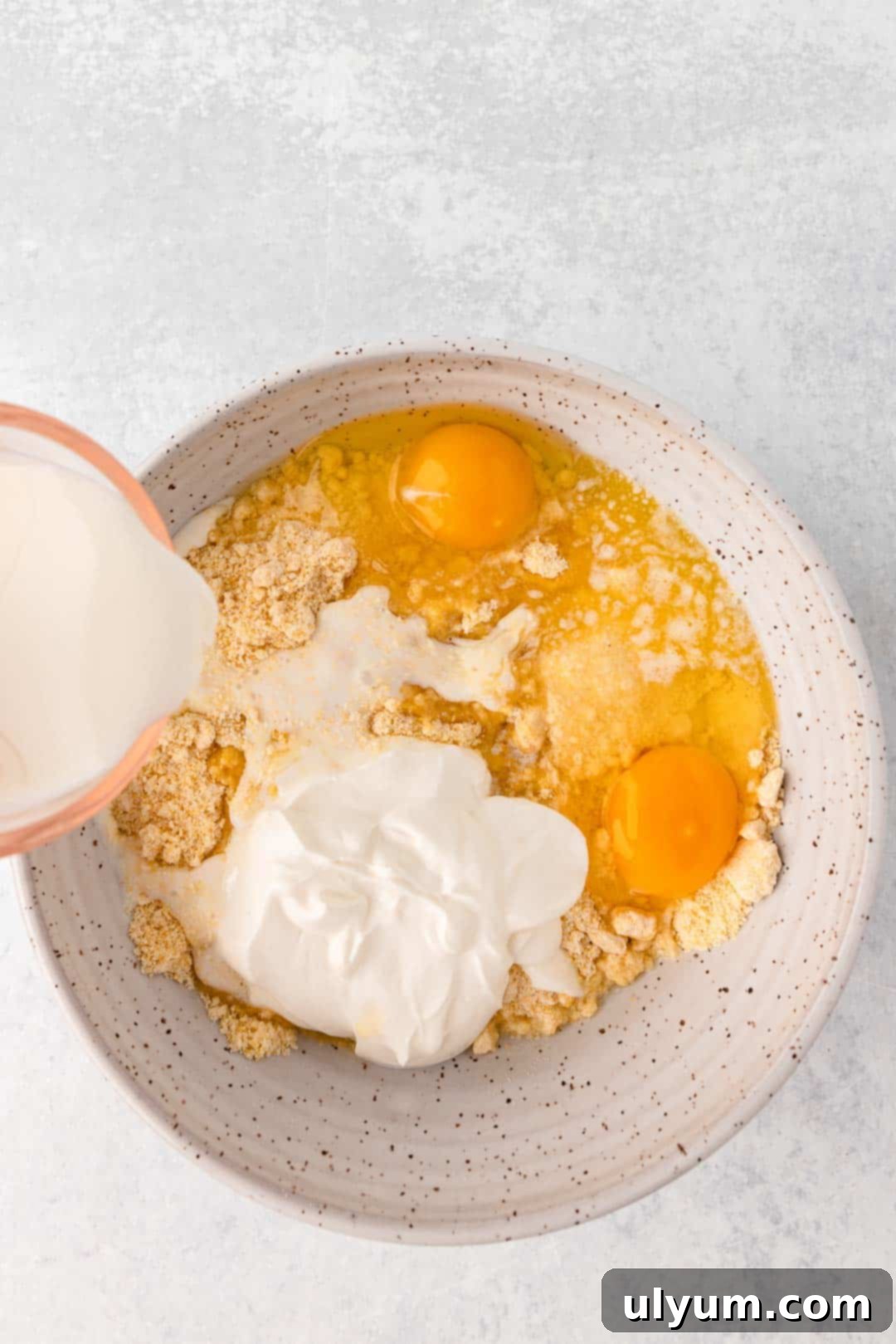 Corn muffin mix, eggs, whole milk, sour cream, and melted butter added to a large mixing bowl for cornbread batter.