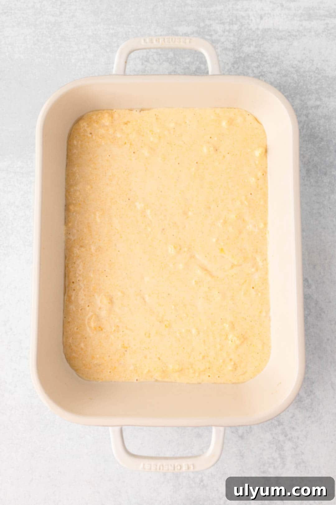 An even layer of cornbread batter is poured into a prepared 9 by 13 inch baking dish, forming the first layer.