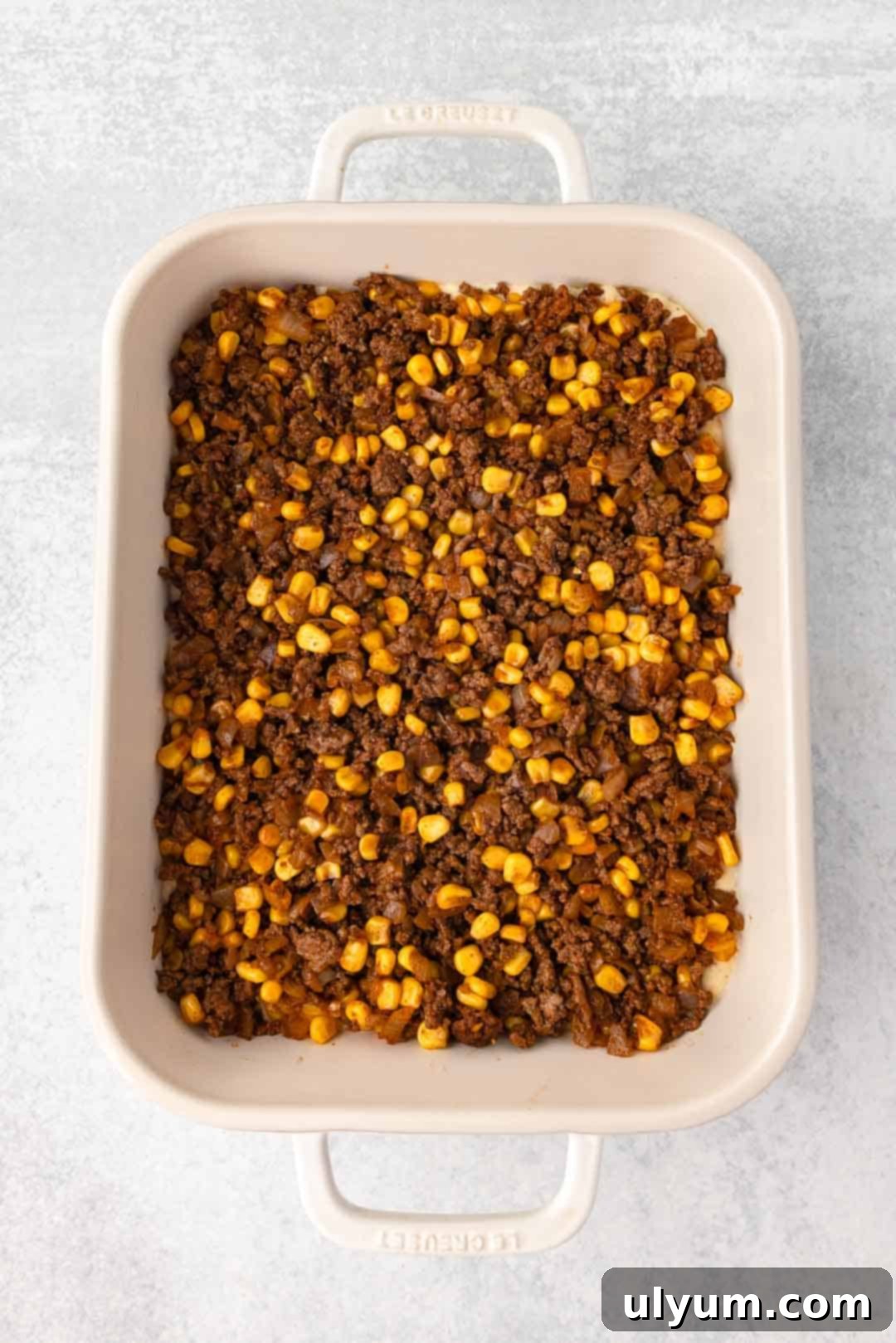 Ground beef mixture is spread evenly over the cornbread batter in the baking dish for the second layer.