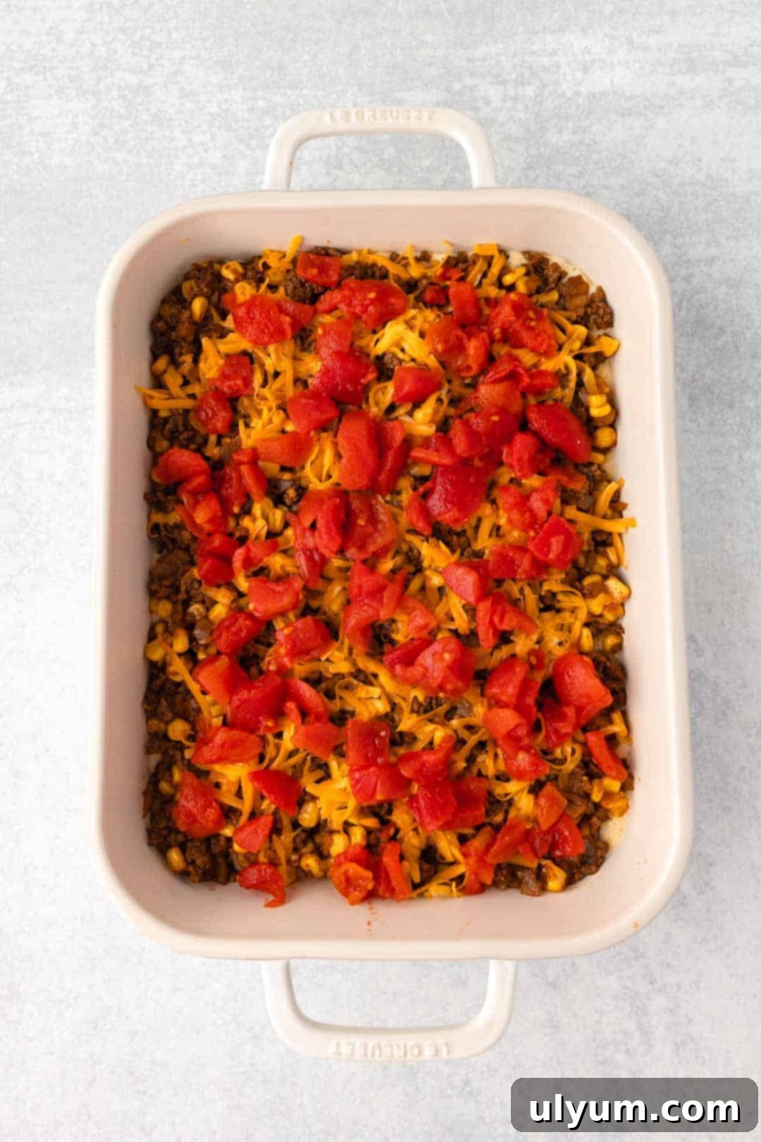 Shredded cheese and drained diced tomatoes are layered over the ground beef mixture, adding flavor and color.