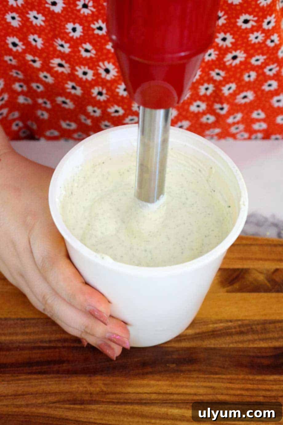 An immersion blender actively blending cottage cheese ranch dip ingredients directly inside the cottage cheese container, showing a convenient and mess-free way to achieve a smooth consistency for this healthy dip.