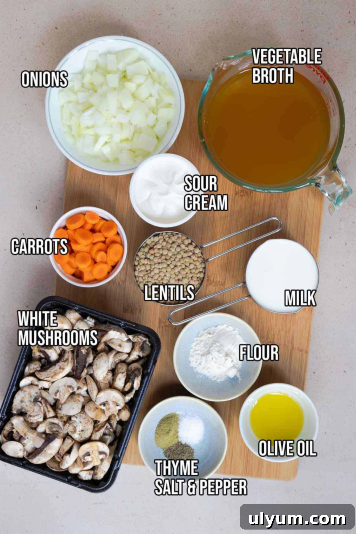 A collection of ingredients for creamy mushroom and lentil soup, including olive oil, various fresh vegetables, dried herbs, lentils, flour, vegetable broth, milk, and sour cream.
