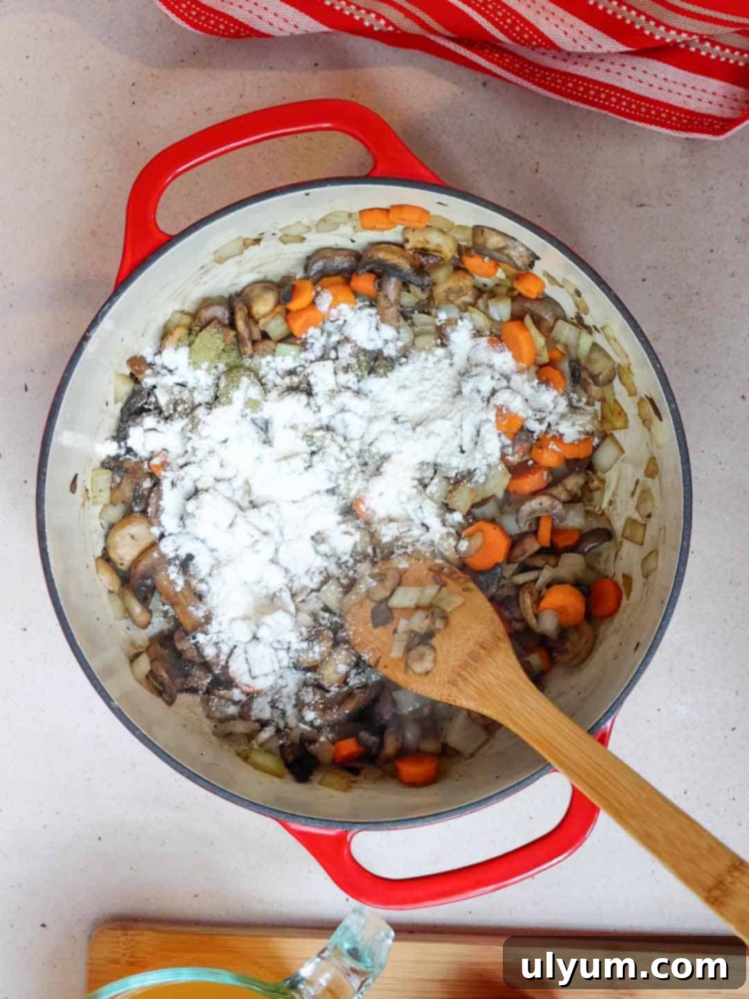 All-purpose flour is sprinkled over the sautéed vegetables in a large pot, ready to be stirred.