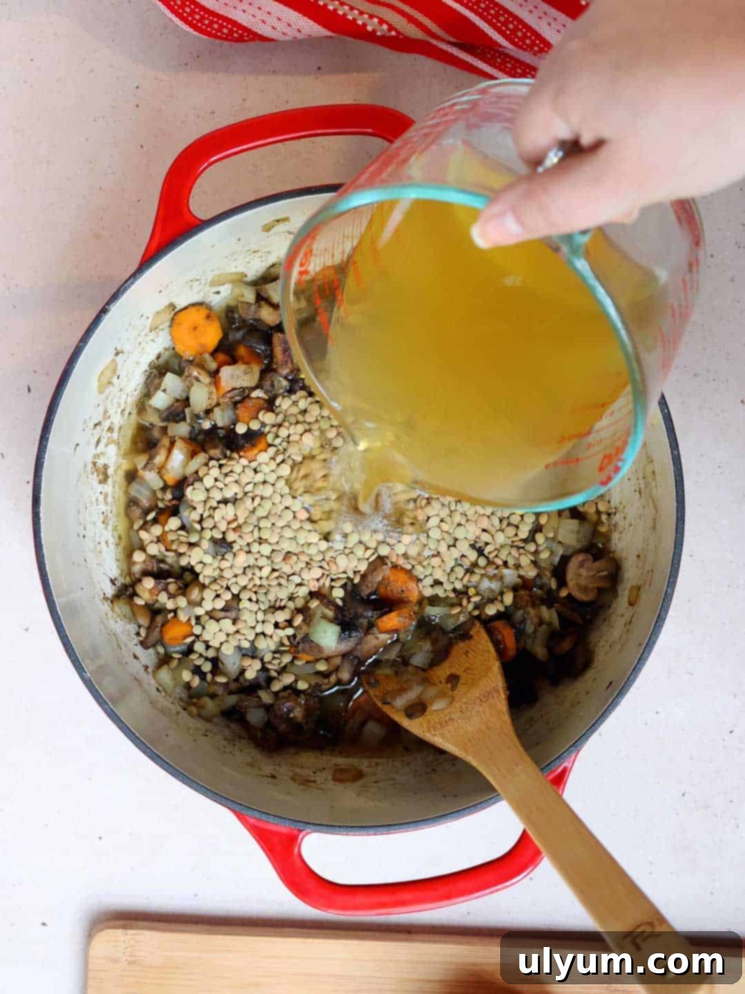 Rinsed brown lentils and vegetable broth being added to the sautéed vegetable mixture in a large pot.
