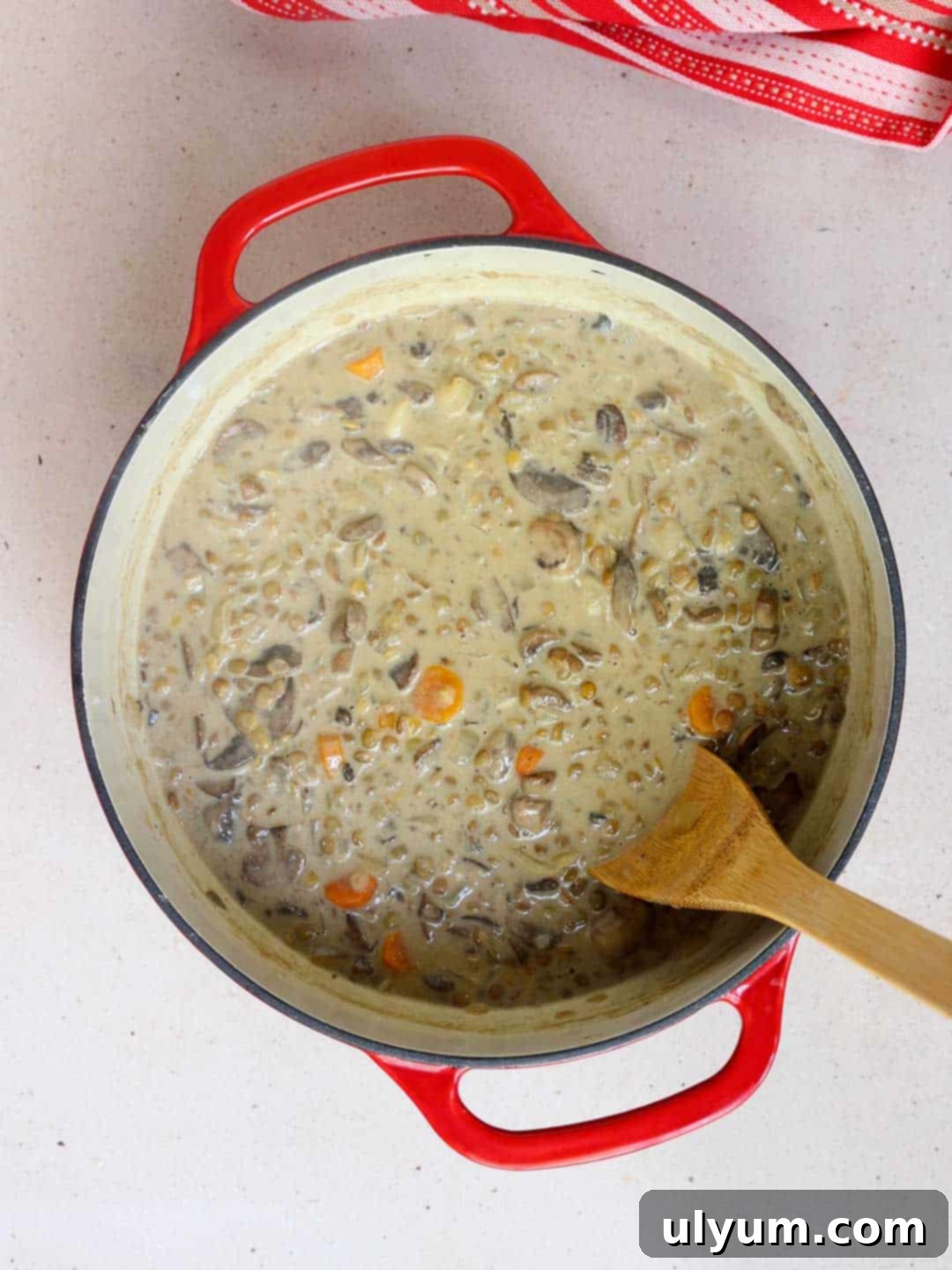 A pot of creamy mushroom and lentil soup with sour cream being stirred in, creating a smooth, rich consistency.