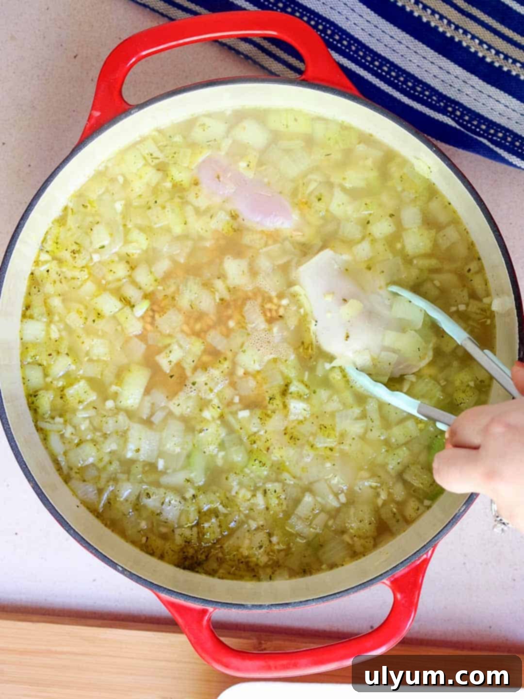 Raw chicken thighs are added to the soup mixture in the large pot using tongs.