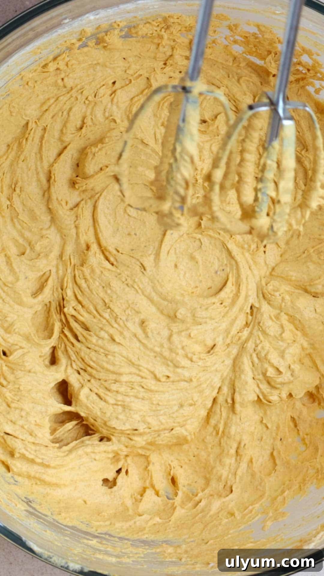 A hand mixer is used to combine the thawed Cool Whip into the pumpkin mixture in the large mixing bowl.