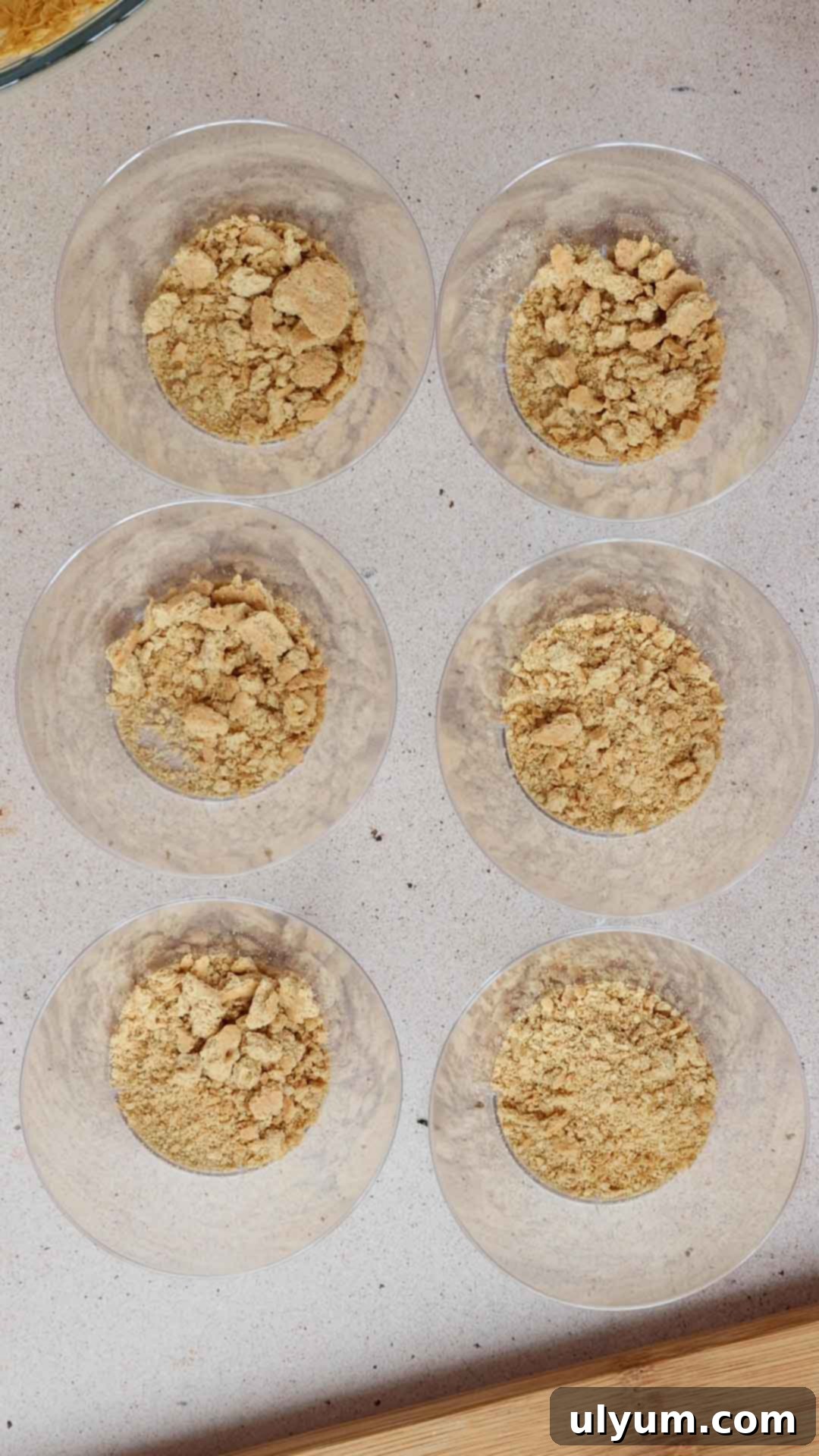 Graham cracker crumbs are added to the bottom of six dessert cups.