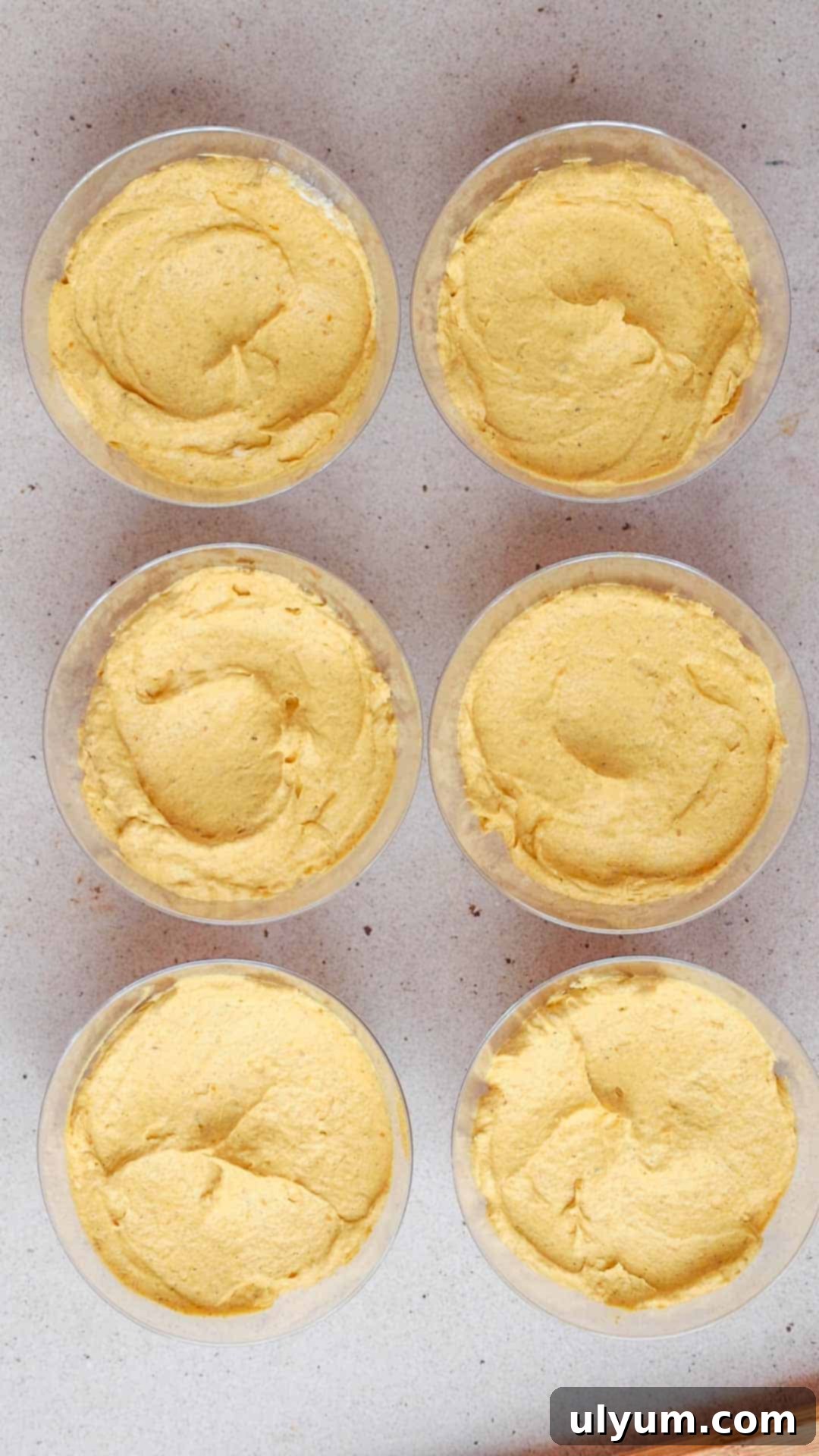 Six dessert cups with pumpkin pie filling inside, smoothed on top with the back of a spoon.