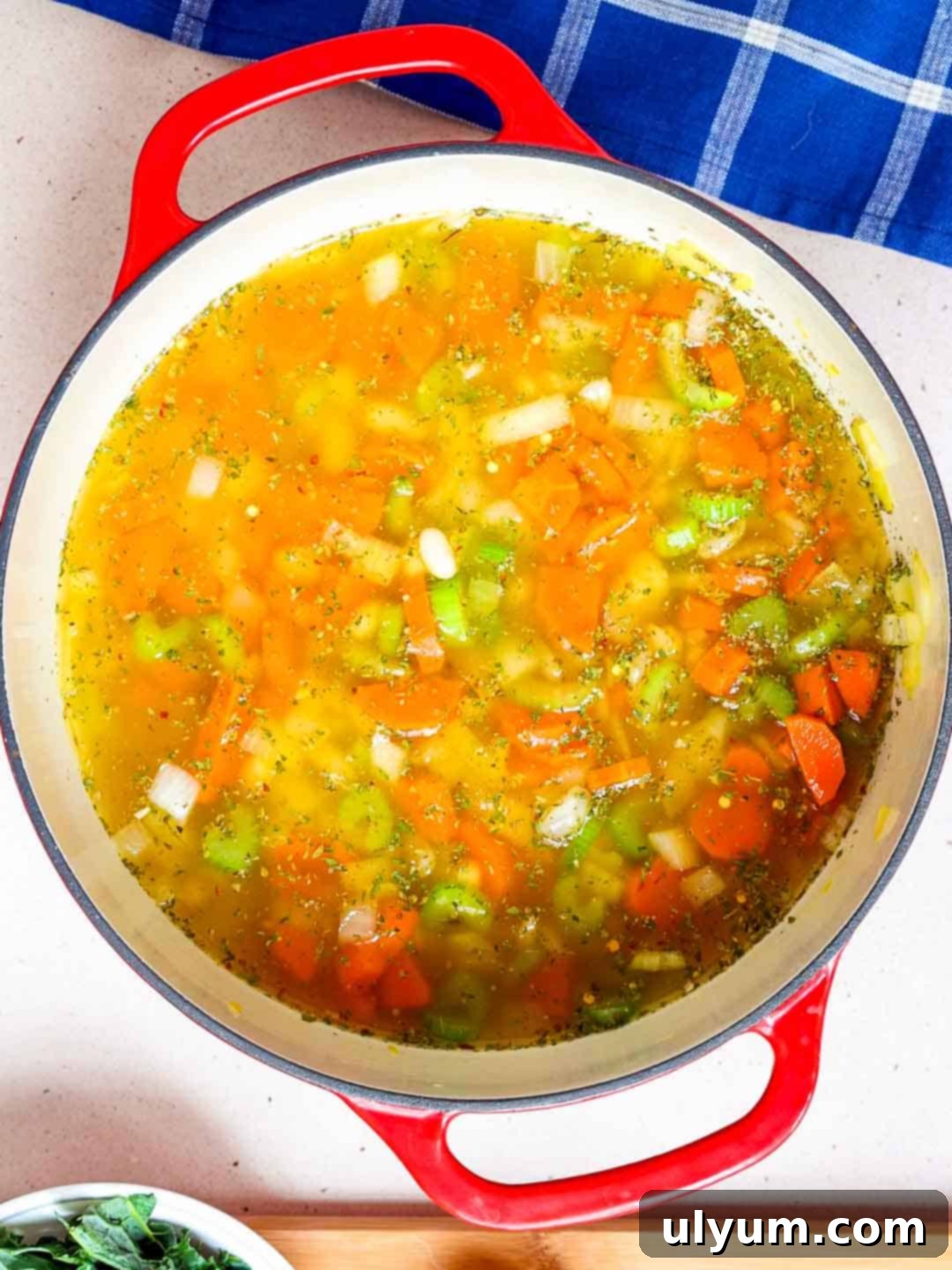 Vegetable broth, drained navy beans, and seasonings are added to a large pot of sautéed vegetables for the soup base.