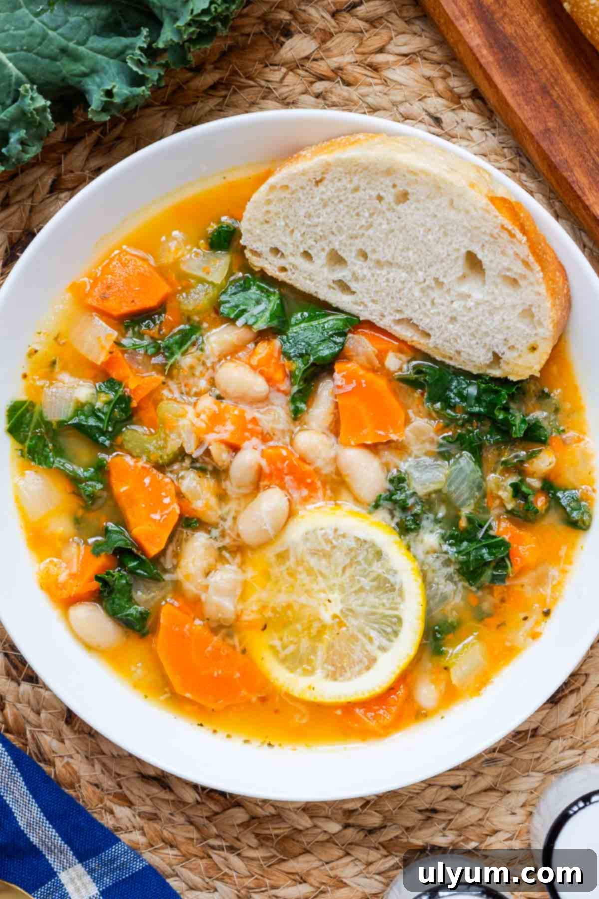 A serving of Lemony White Bean Soup with Kale in a small bowl, garnished with grated Parmesan cheese and served with a slice of crusty bread.