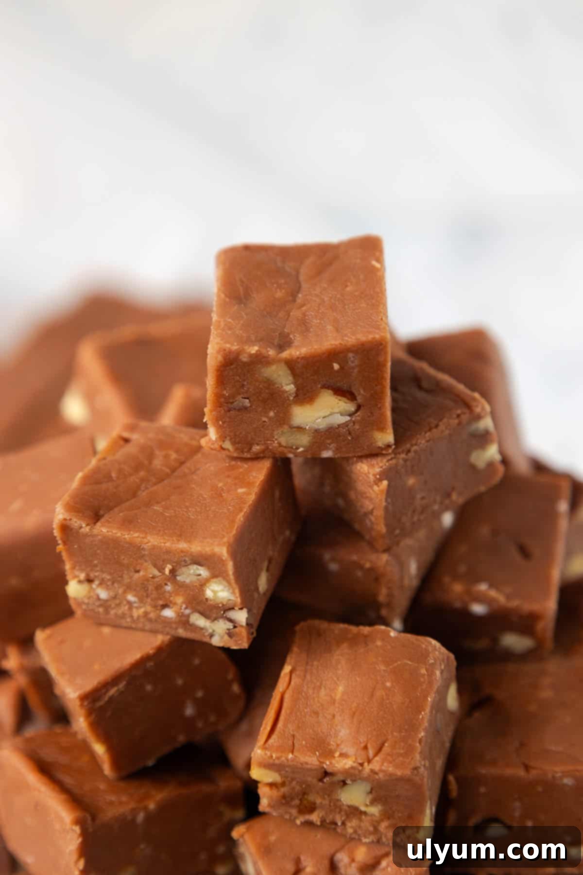 One inch squares of Velveeta fudge with pecans stacked on a small plate, showcasing their smooth texture and nutty inclusions.