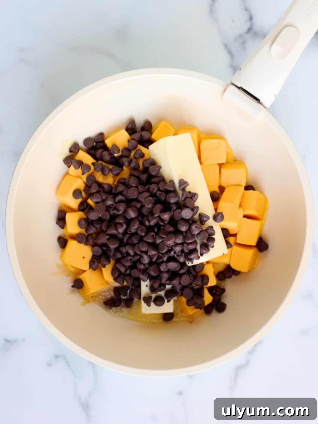 Cubes of Velveeta, butter, chocolate chips, and light corn syrup are placed in a large pot, ready to be melted over medium heat.