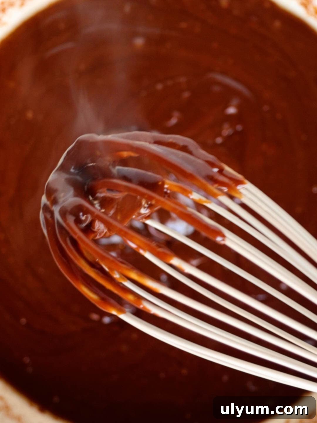 The chocolate cheese mixture in the large pot is fully melted and whisked into a smooth, glossy consistency, ready for the next steps.