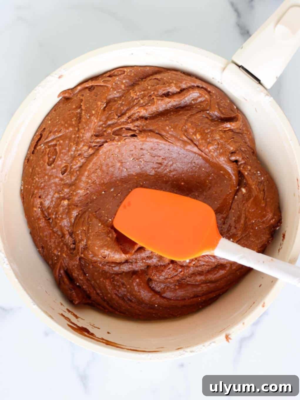 Chopped pecans are being stirred into the rich, melted chocolate fudge mixture in a large pot with a silicone spatula.