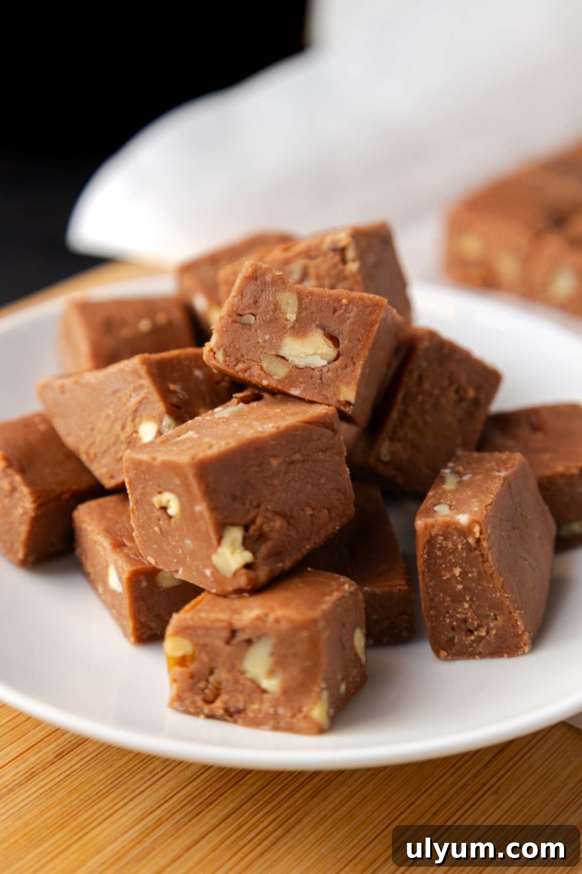 Several neatly cut 1-inch squares of Velveeta fudge with pecans are stacked artfully on a small plate, ready for serving.