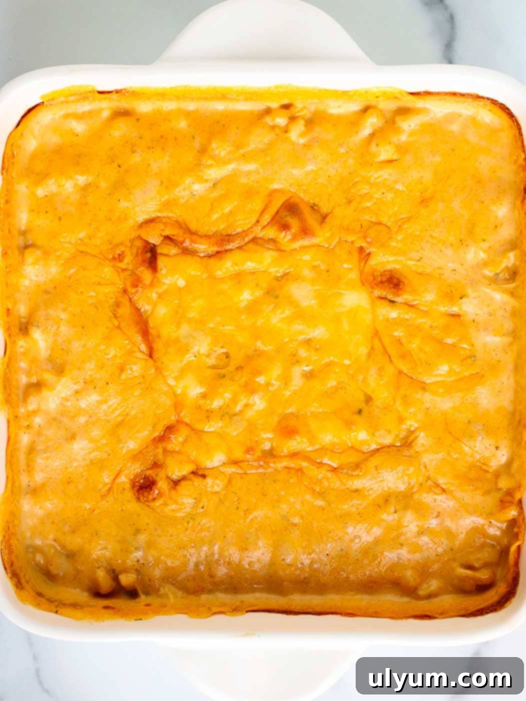 Cheesy corn casserole baked in an 8 by 8 inch baking dish with a layer of melted cheese on top.