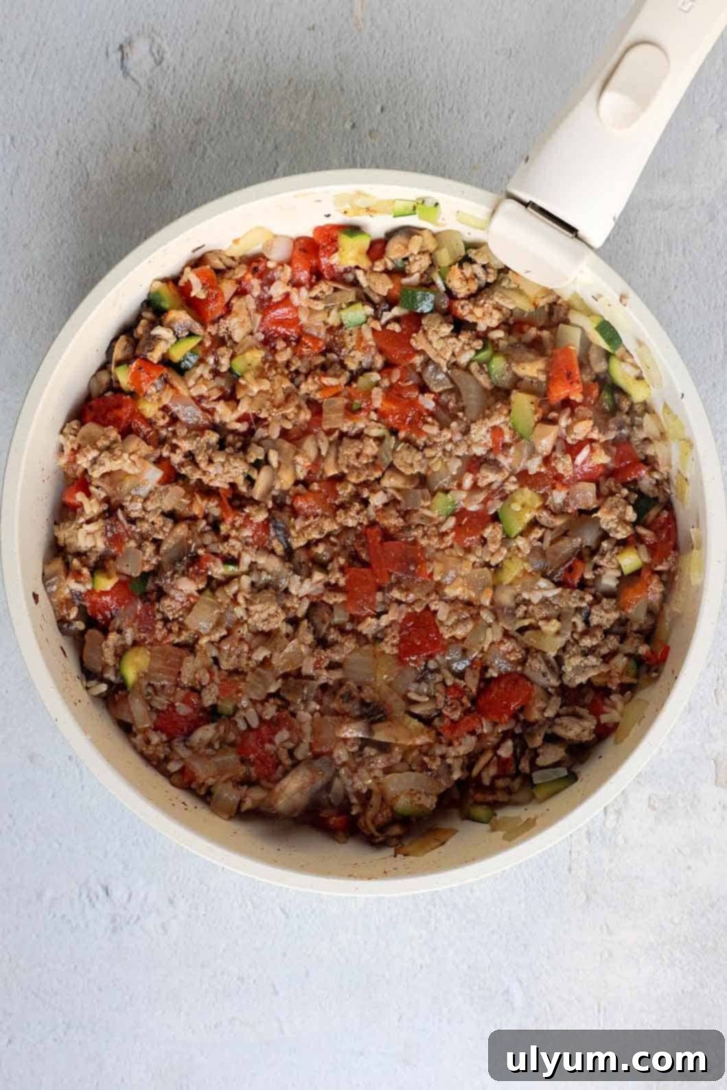Hearty Ground Turkey and Rice Stuffed Peppers 7 The ground turkey mixture in a skillet, now enriched with diced onion, mushrooms, zucchini, fire-roasted tomatoes, cooked rice, and a medley of seasonings, is being stirred to combine all the delicious components for the stuffed peppers.