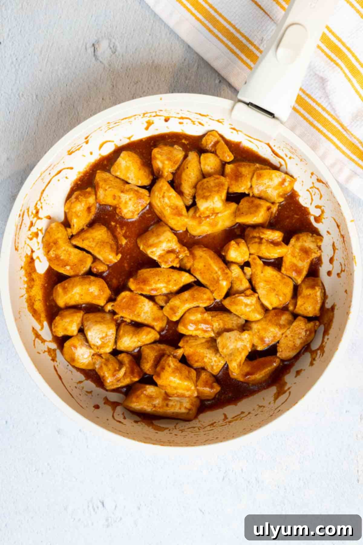 Cooked diced chicken in a large skillet seasoned and coated in sauce.
