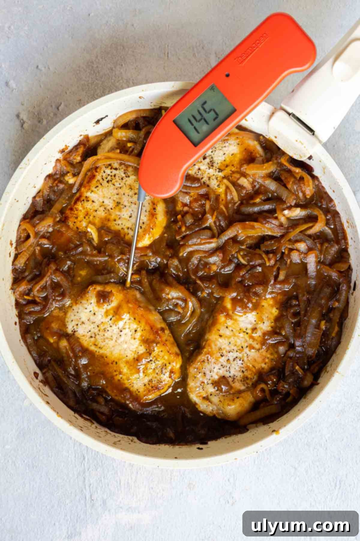 Savory French Onion Pork Chops 11 A meat thermometer in a pork chop showing 145°F, with the chops simmering in caramelized onions.