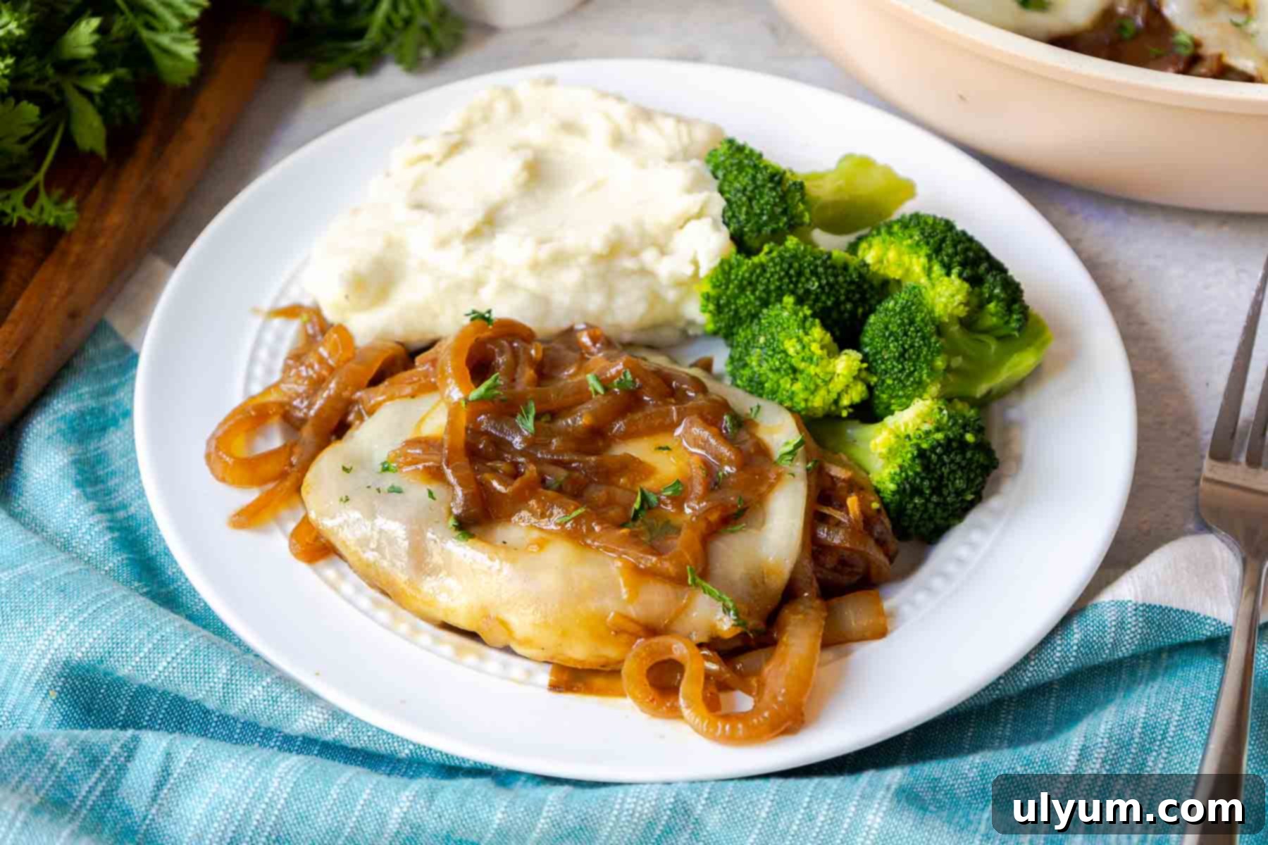 Savory French Onion Pork Chops 15 A pork chop topped with onions and cheese on a plate with mashed potatoes and broccoli.