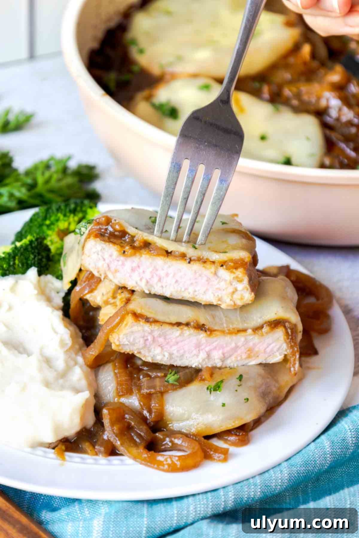 Savory French Onion Pork Chops 3 A sliced pork chop topped with onions and cheese on a plate with mashed potatoes and broccoli.