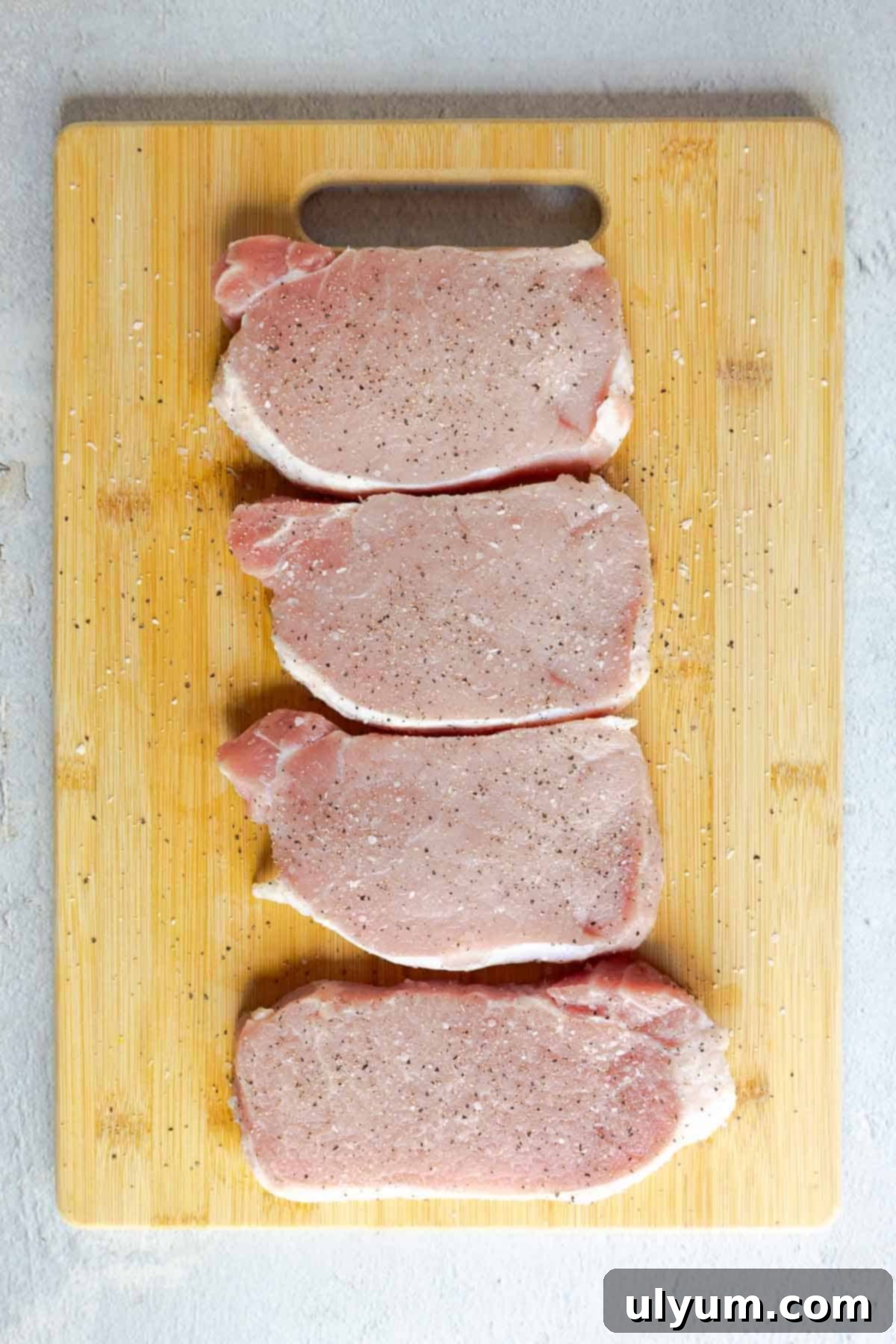 Savory French Onion Pork Chops 5 Four raw pork chops seasoned with salt and pepper on a wooden cutting board.