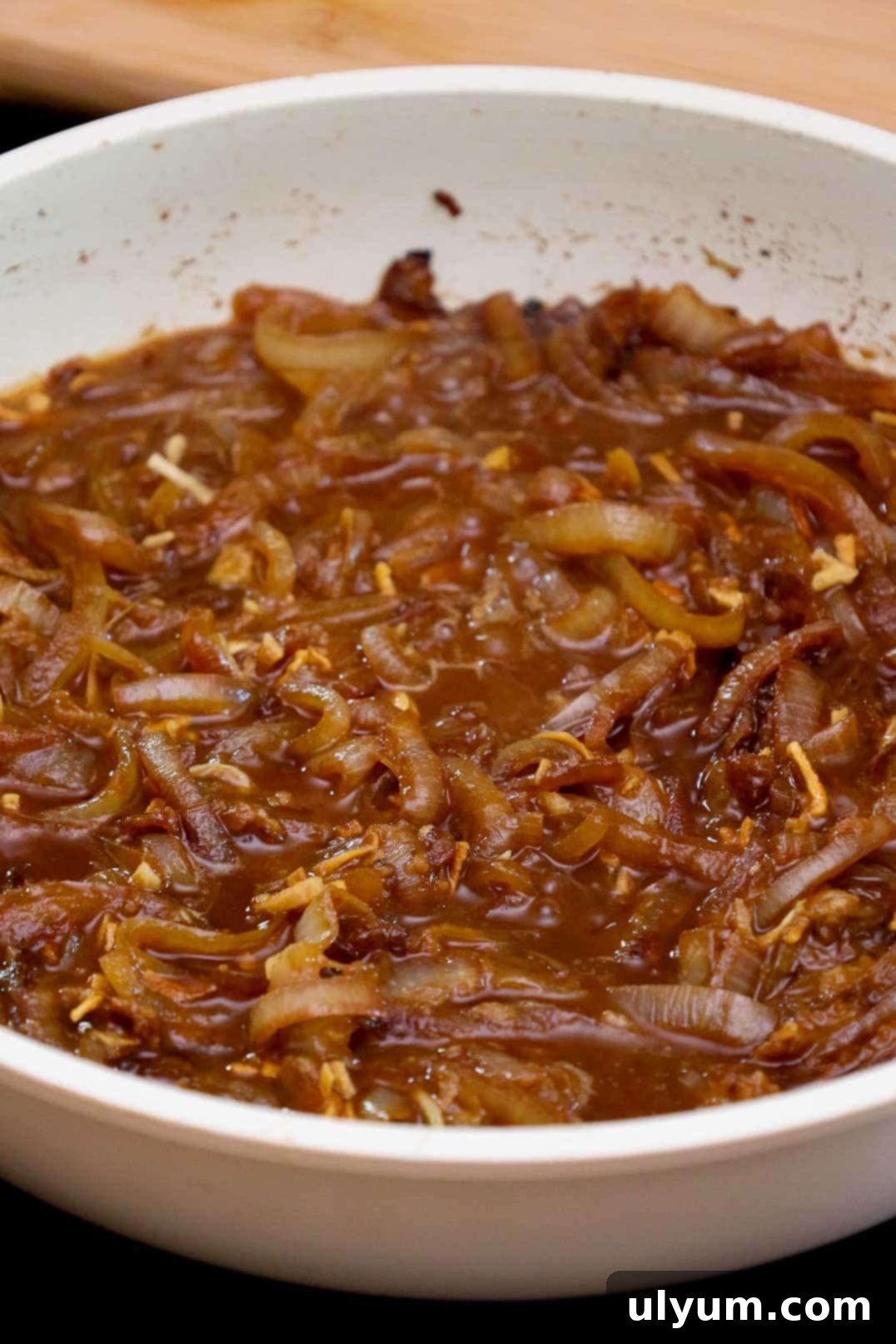 Savory French Onion Pork Chops 9 Caramelized onions simmering in broth in a white skillet.