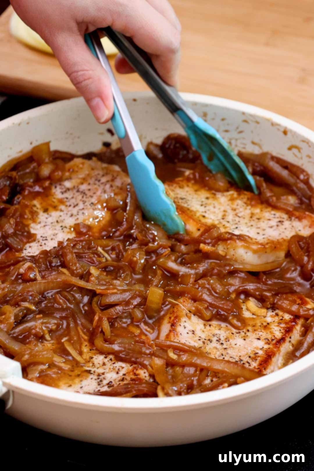 Savory French Onion Pork Chops 10 Tongs placing pork chops into a skillet with caramelized onion sauce.