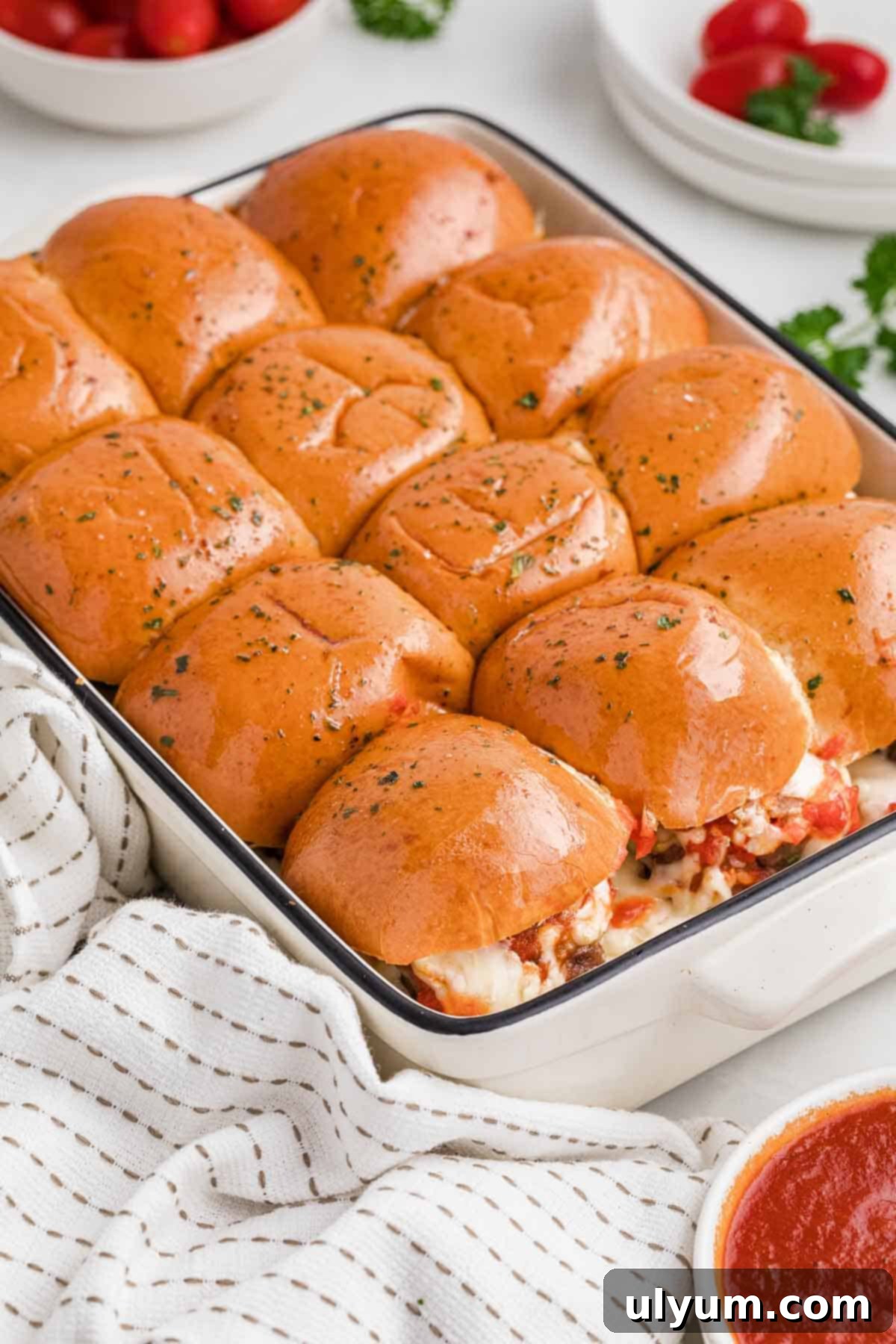A baking dish filled with golden brown sliders topped with butter and seasonings.