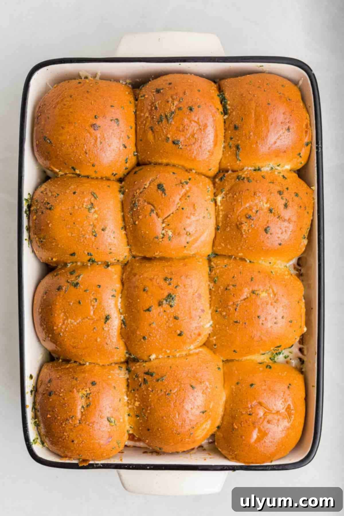 A pan of baked sliders with golden brown tops and herbs.