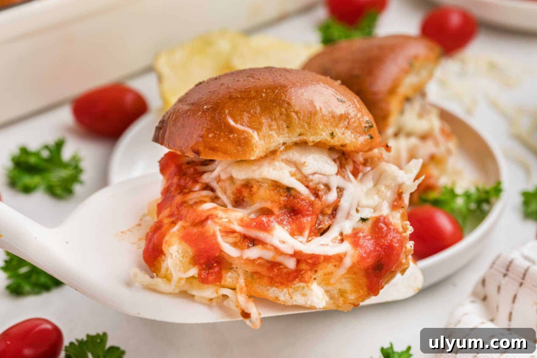 A cheesy meatball slider on a spatula, topped with marinara sauce.